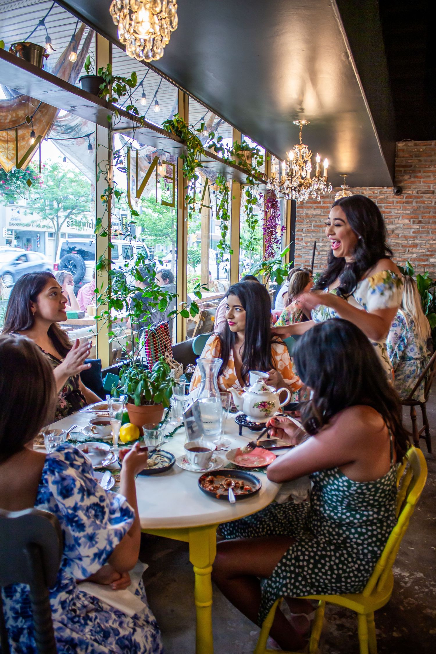 Toronto Event Photographer - Bright restaurant scene with hanging plants, chandeliers and yellow chairs around dining tables.