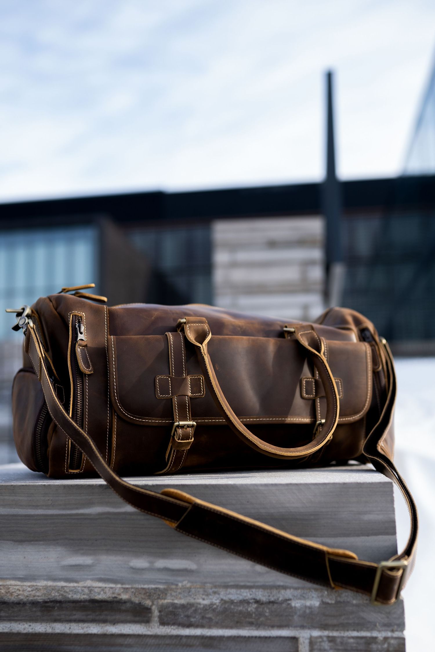 Toronto Product Photographer - Rustic brown leather duffle bag with shoulder strap displayed on concrete steps.