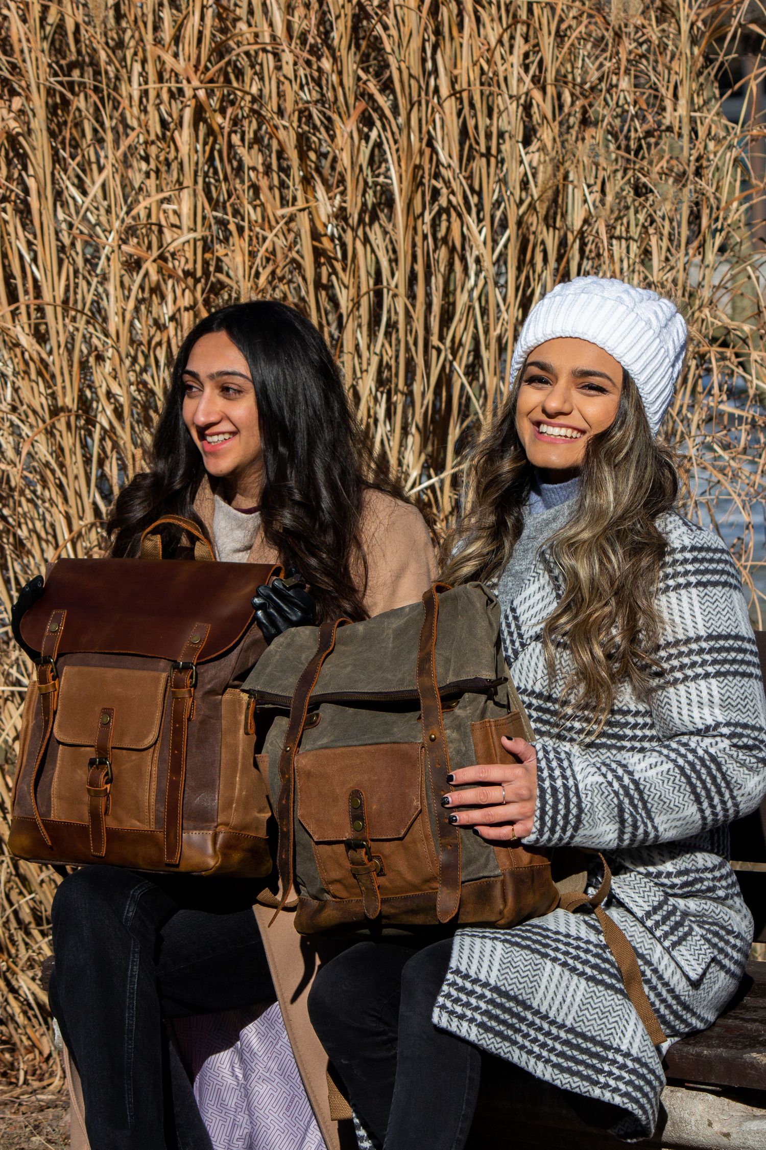 Toronto Portrait Photographer - Two people showcase brown leather backpacks against dried grass backdrop in winter clothing.