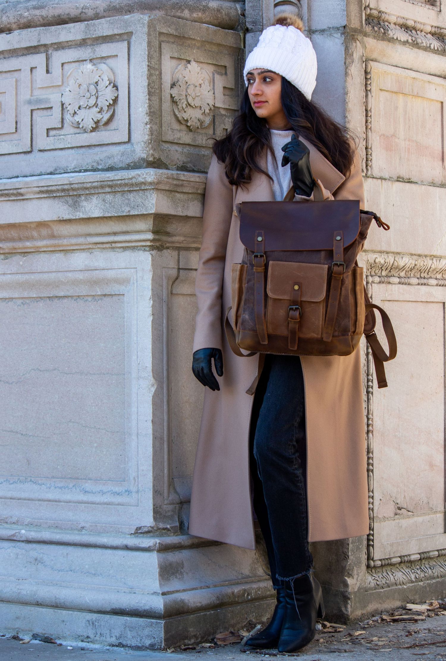 Toronto Portrait Photographer - Winter fashion look with beige coat, leather backpack and white beanie against stone architecture.