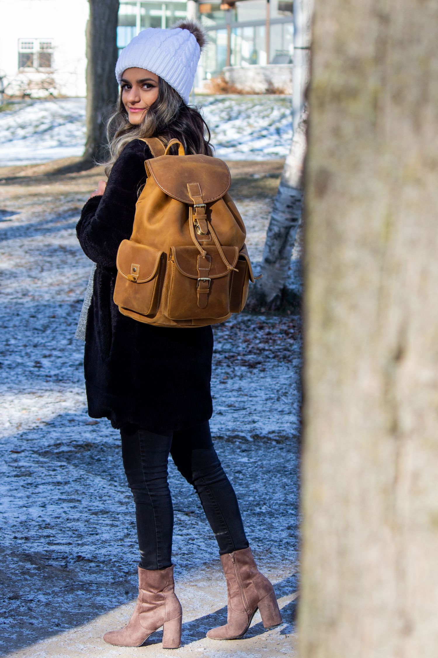 Toronto Portrait Photographer - Person models a brown leather backpack with winter accessories and ankle boots in snowy setting.