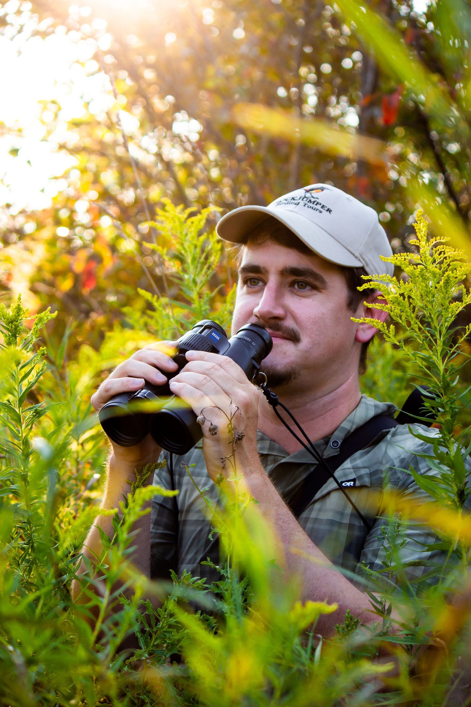Toronto Portrait Photographer - Wildlife observer using binoculars in golden sunlit natural setting with foliage.