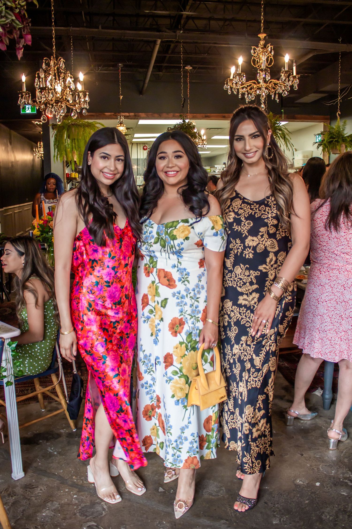 Toronto Event Photographer - Three people in colorful dresses pose at an event venue decorated with elegant crystal chandeliers.