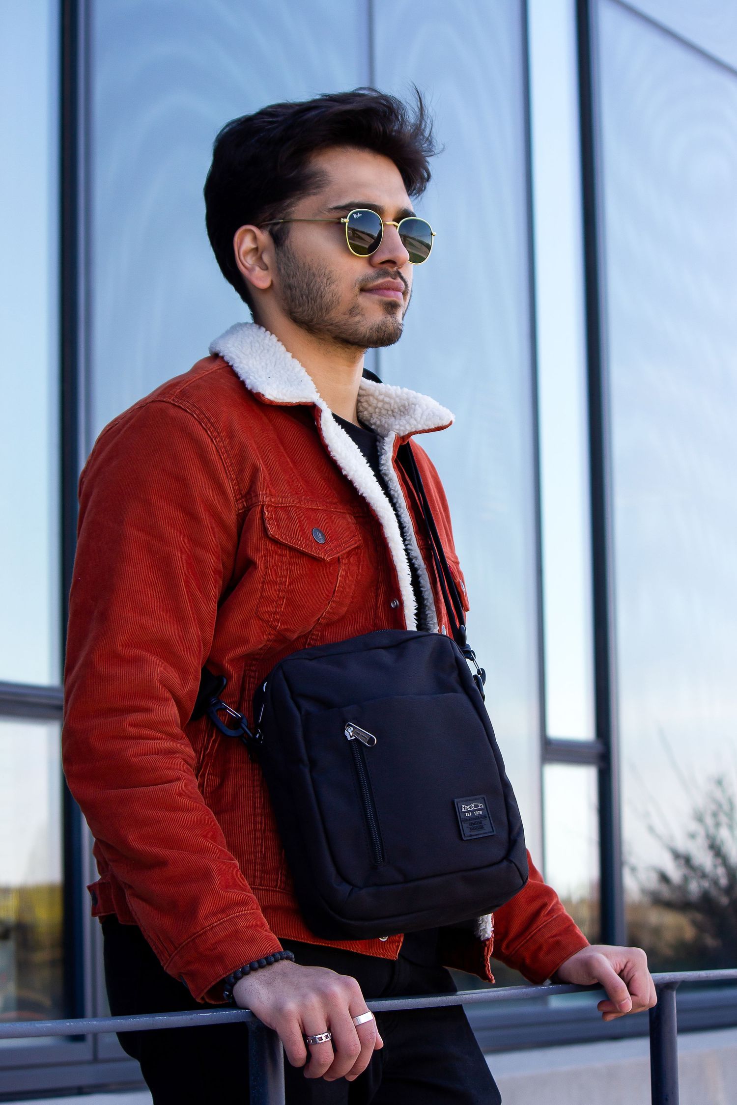 Toronto Portrait Photographer - Person wearing red sherpa jacket and sunglasses with black messenger bag against glass building.