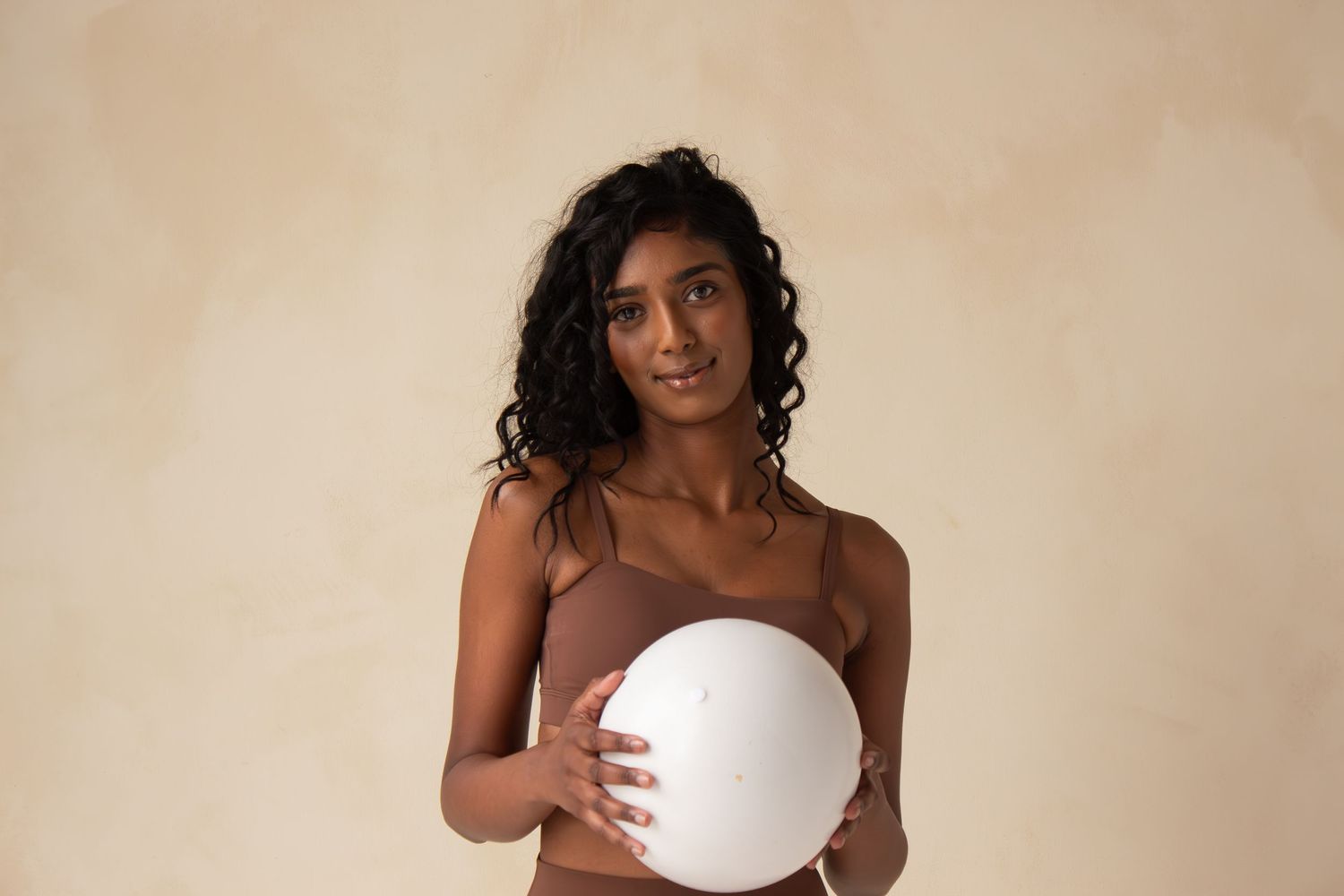 A person in a neutral studio setting holds a white circular disc against a beige background.