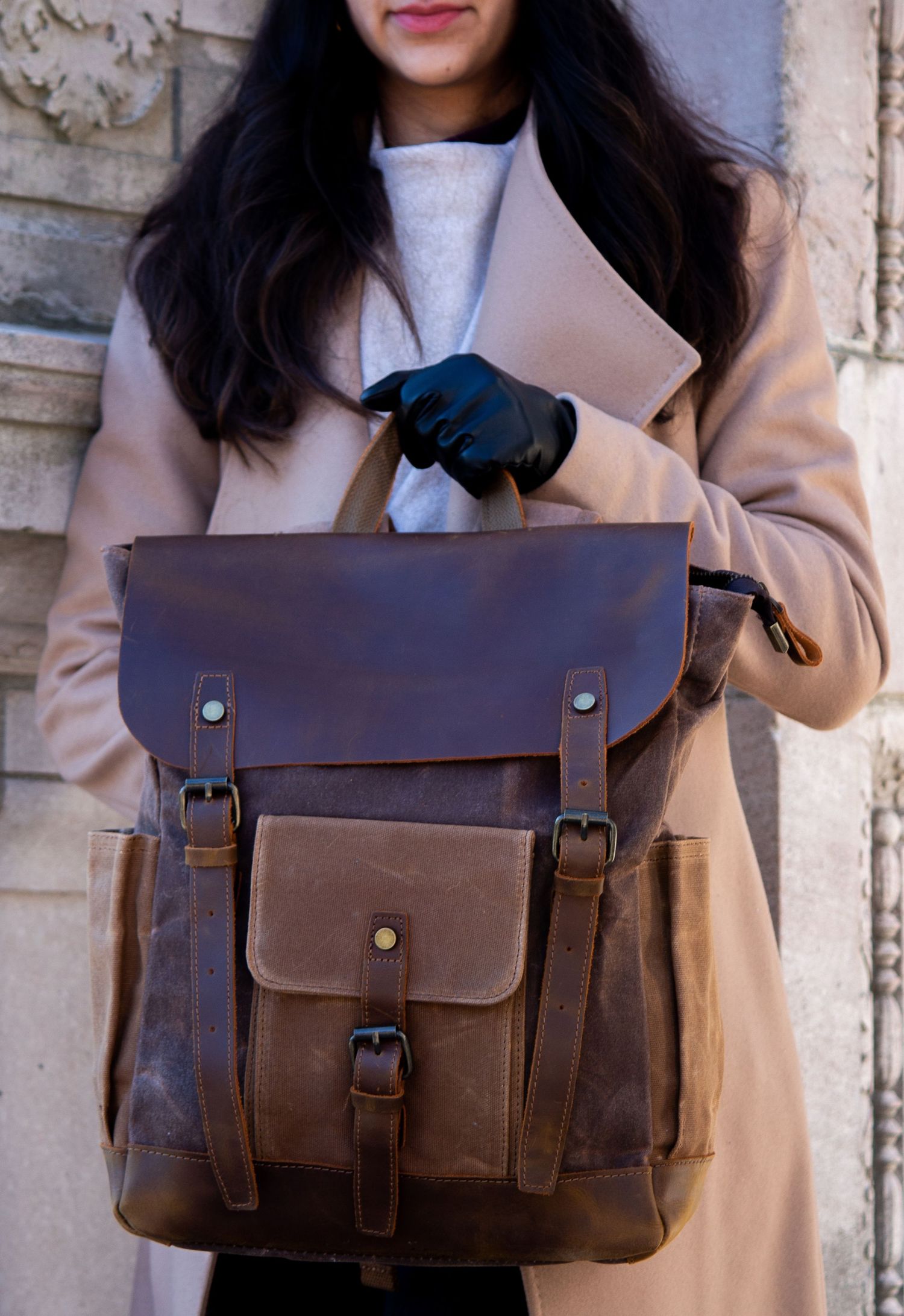 Toronto Product Photographer Stylish brown leather backpack with buckle details and front pocket being held by someone wearing a beige coat.