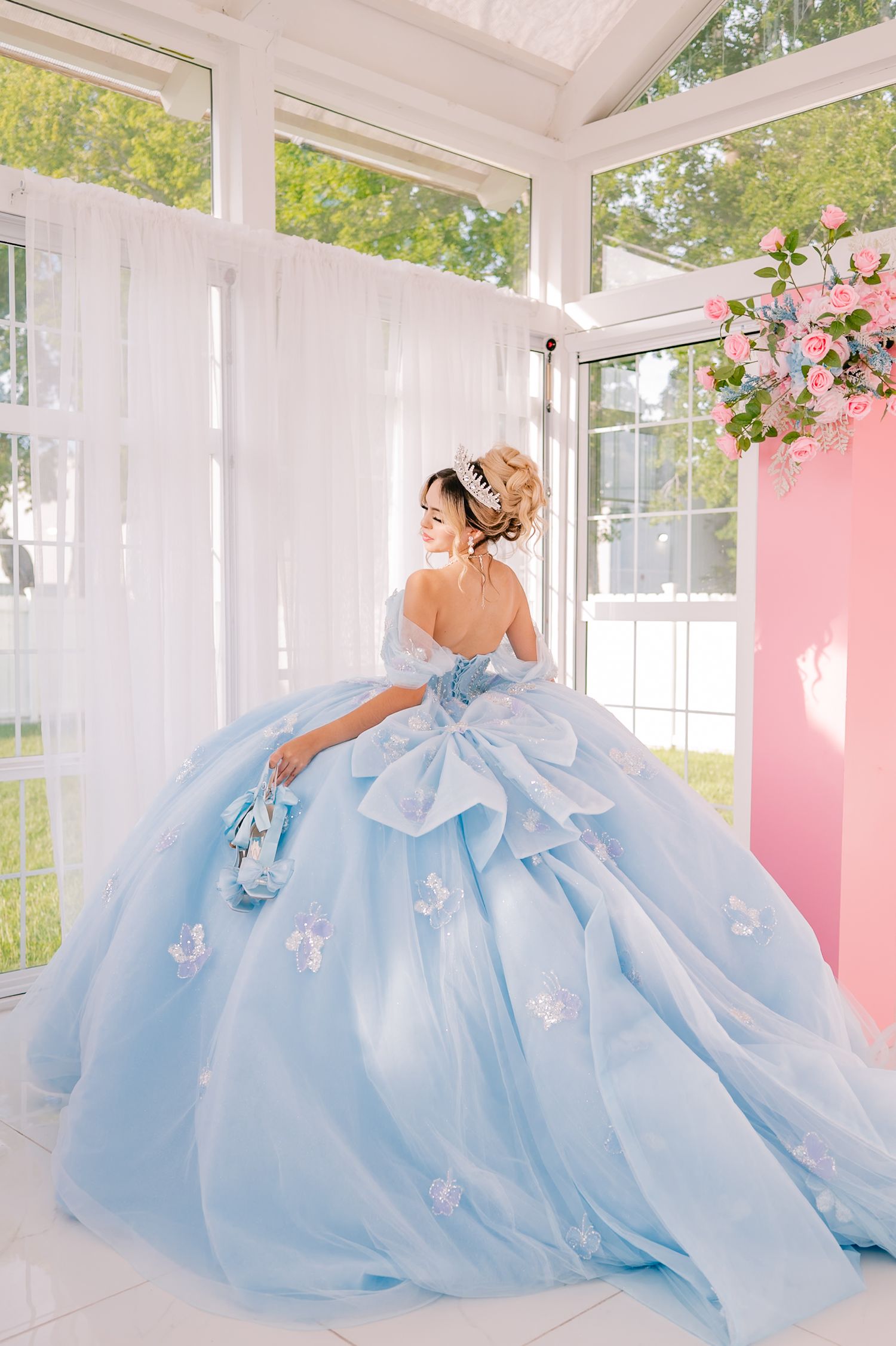 A flowing light blue ballgown photographed in a white conservatory with pink floral accents.