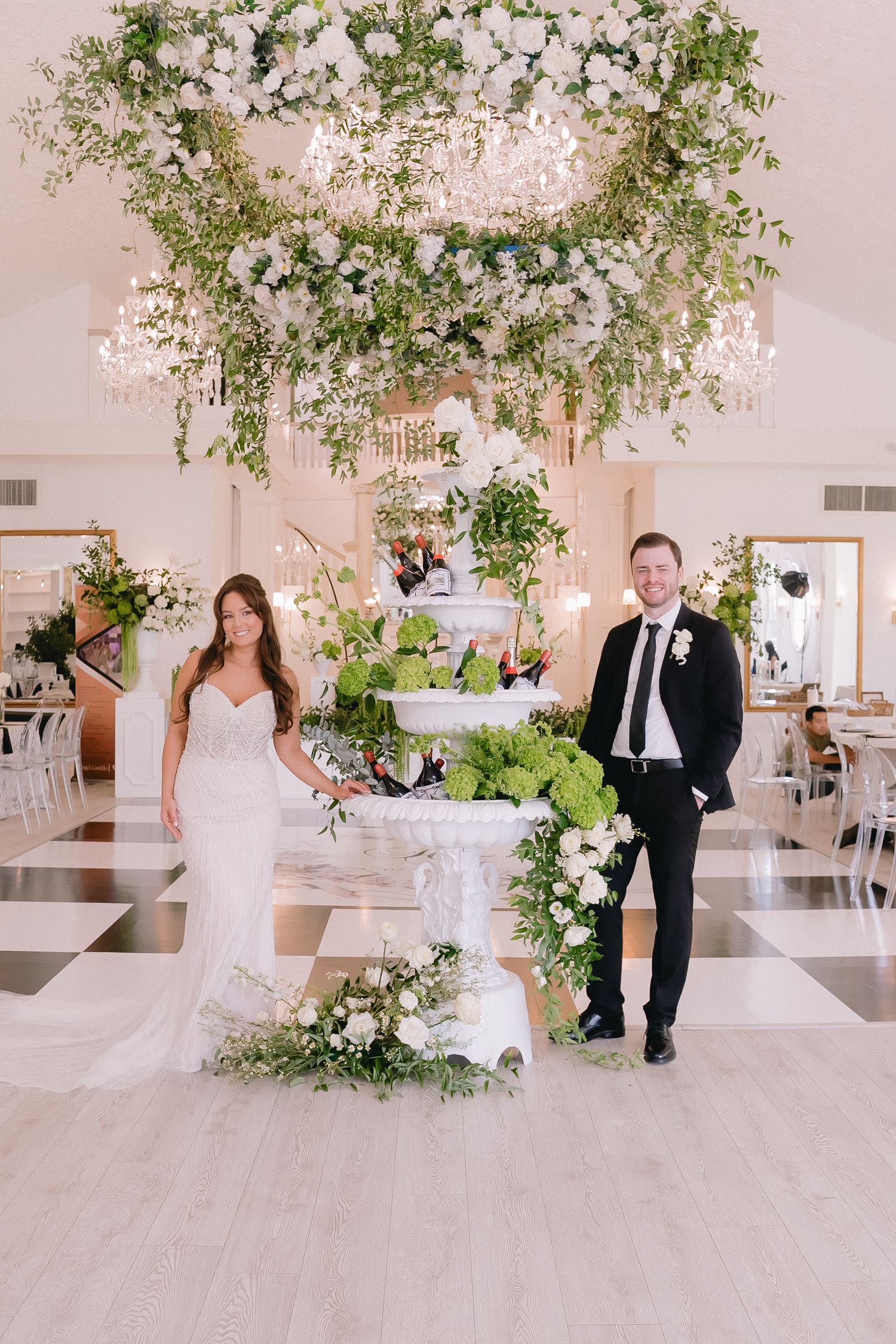 Light-filled wedding space featuring lush floral arches and white decor elements.
