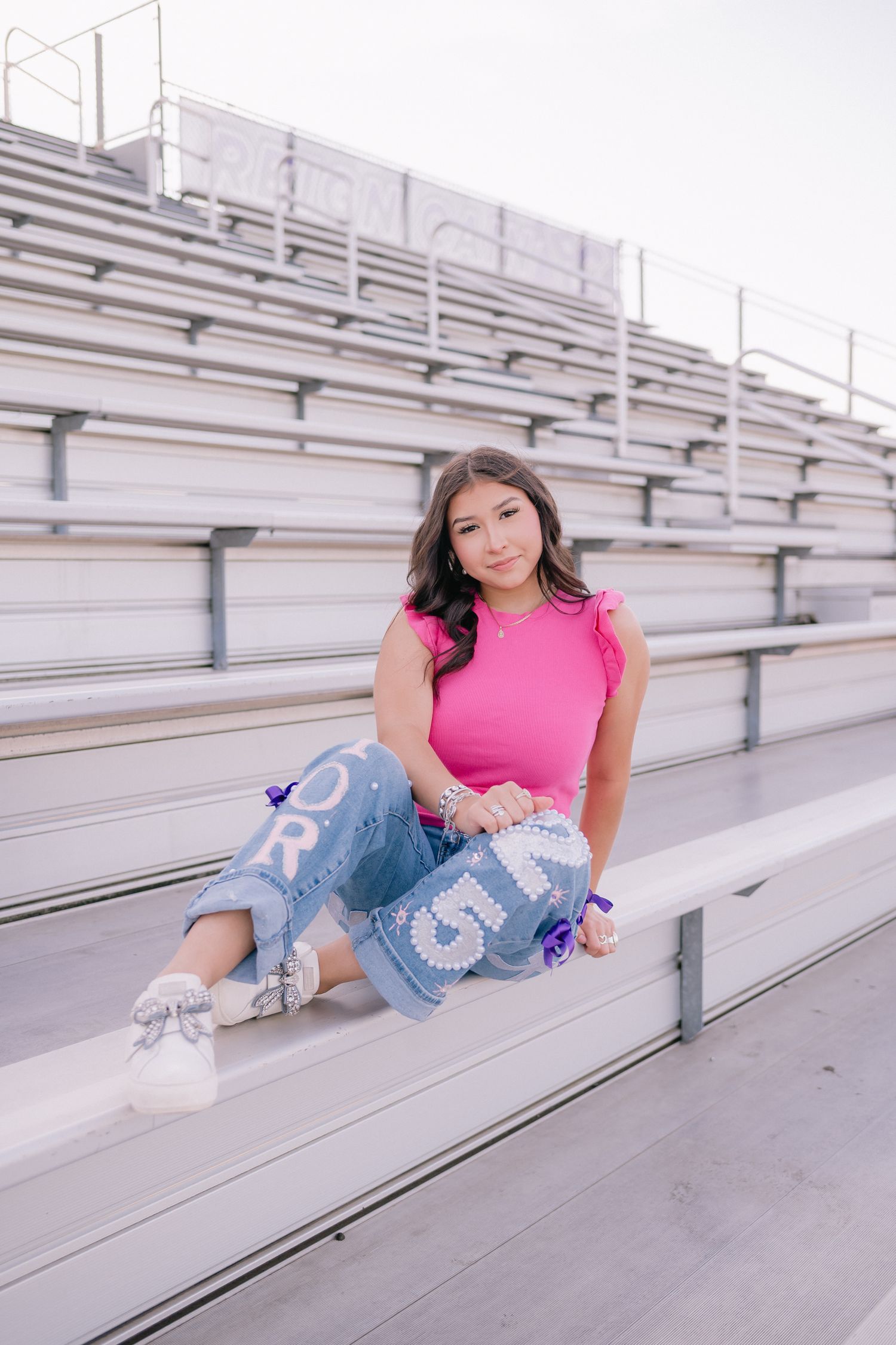 Casual portrait session on bleachers wearing pink top and decorated jeans.