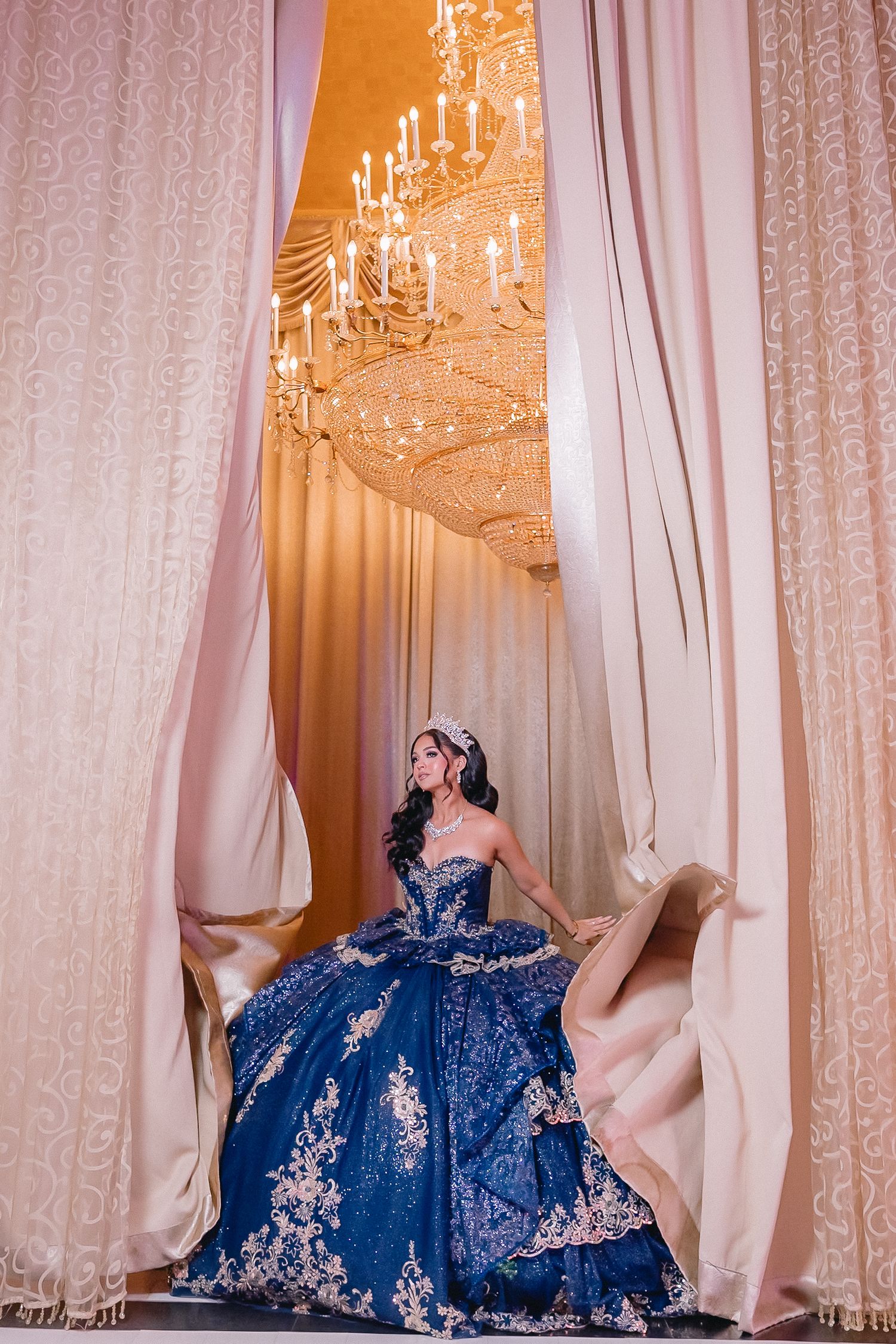 Blue ballgown dress displayed under crystal chandelier in elegant venue.