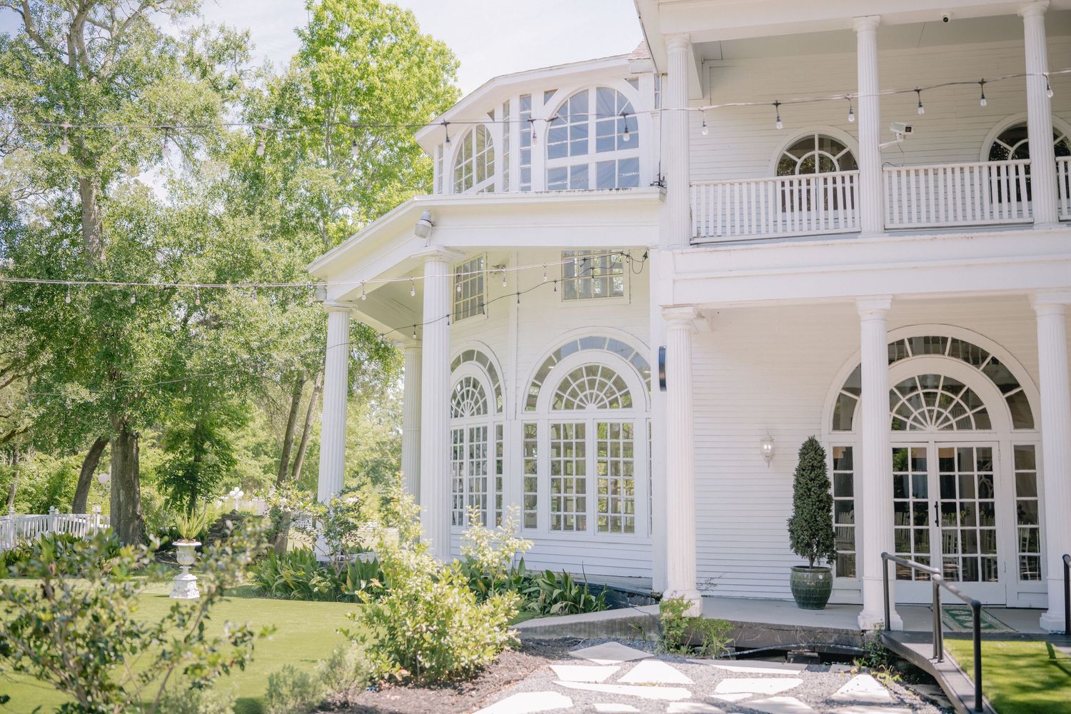 An elegant white wedding venue exterior featuring classic colonial architecture and manicured grounds.