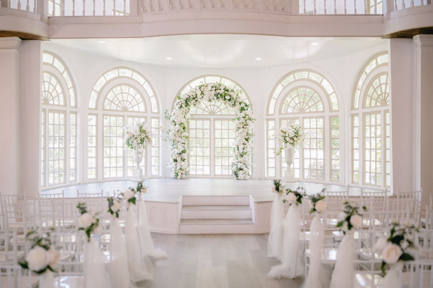 An elegant white conservatory venue decorated with floral arrangements and classic architectural details.