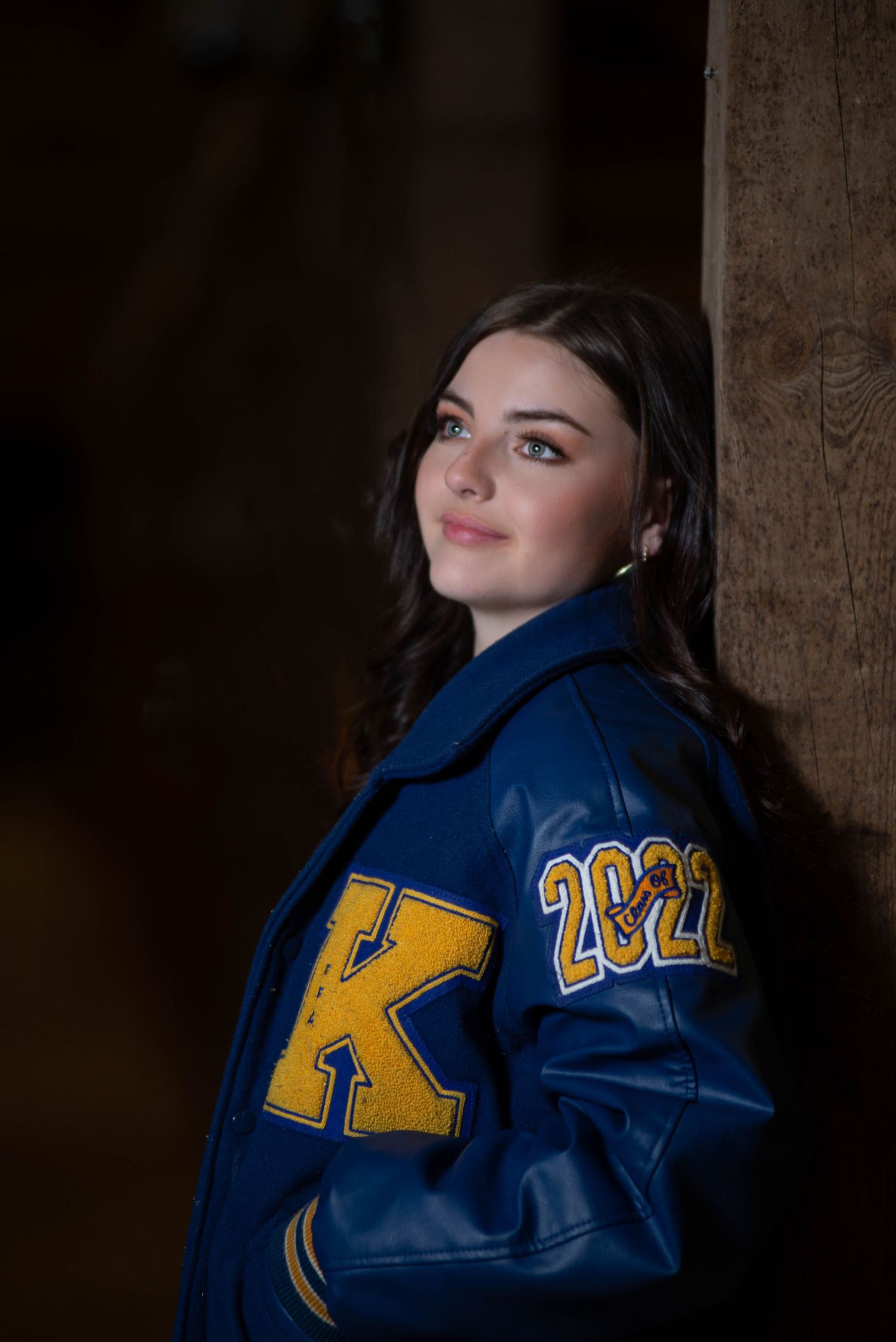 A blue varsity jacket with 2022 lettering photographed in a dimly lit barn.