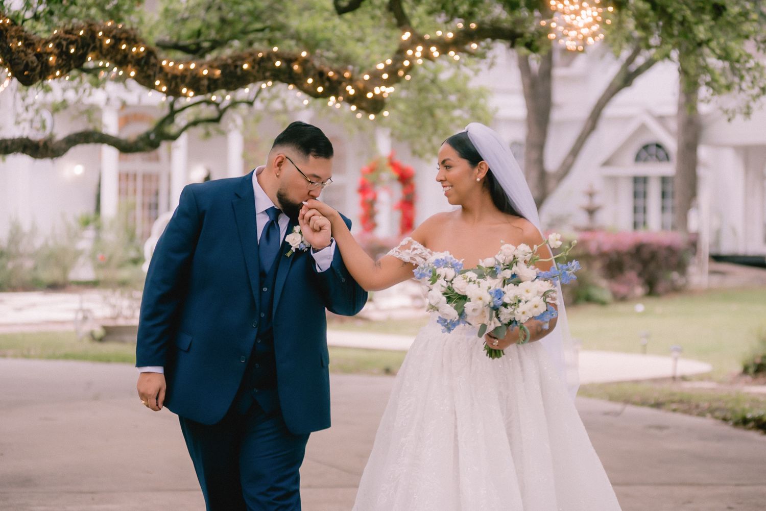Wedding couple sharing an emotional moment under trees with string lights at dusk.