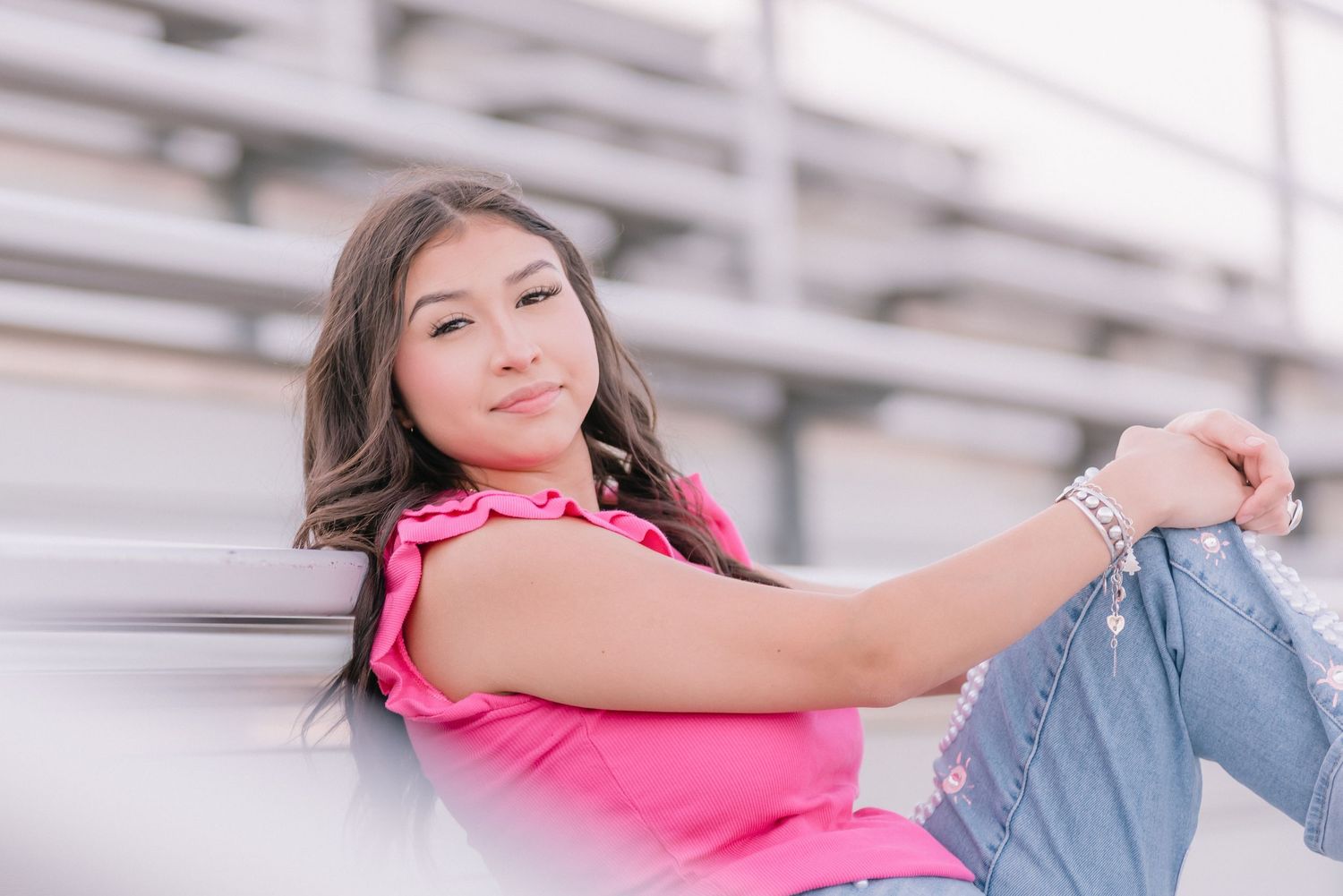 Casual senior photo on stadium bleachers in bright pink top.