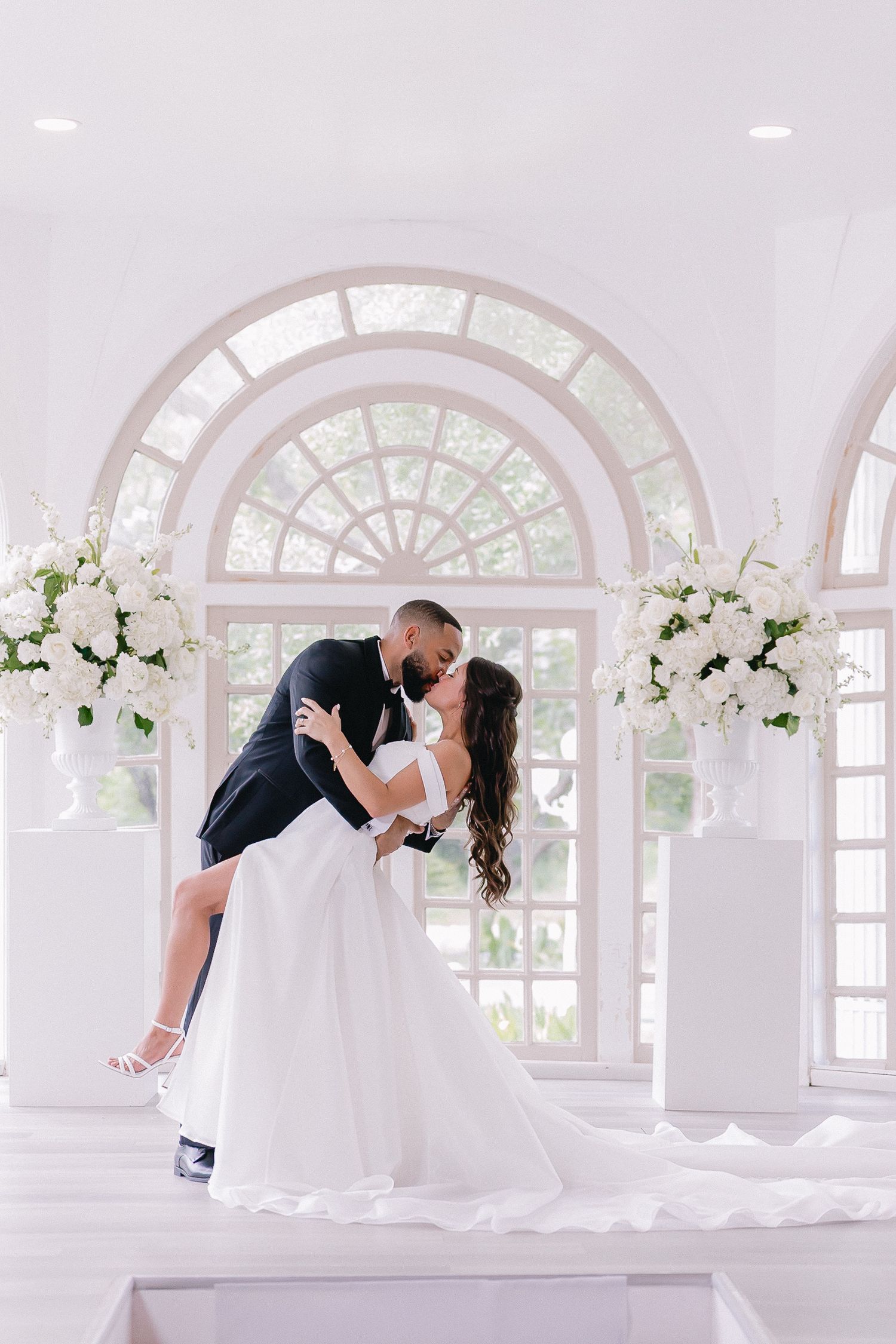 Romantic wedding portraits in white arched sunroom with elegant floral arrangements.