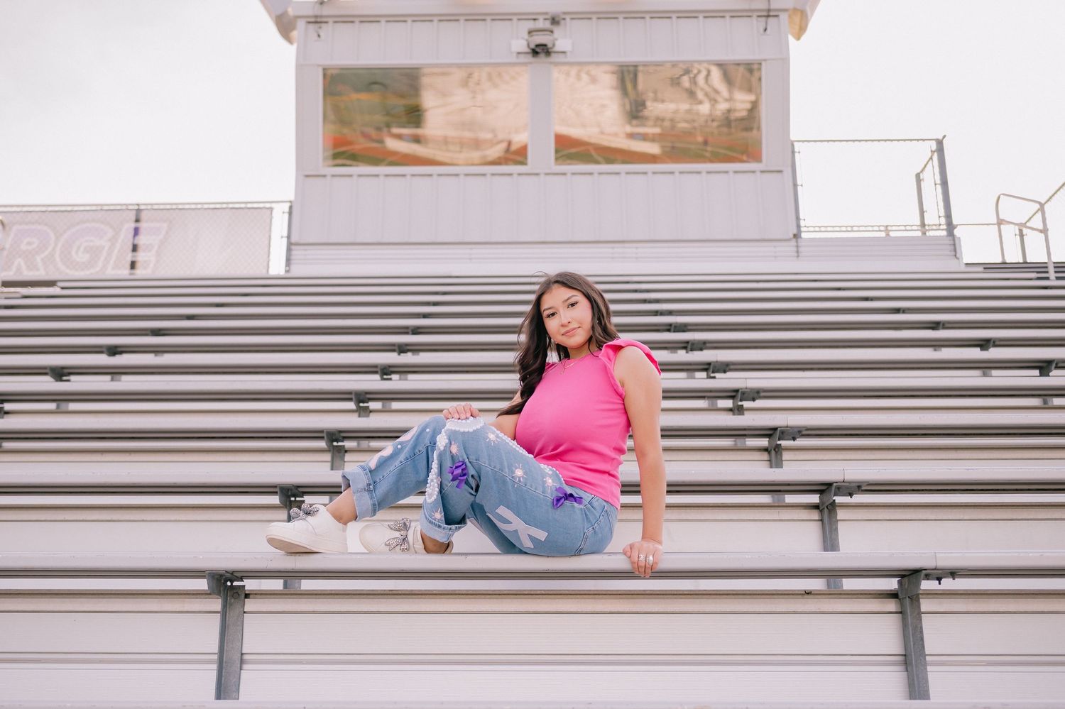 Senior portrait on bleachers wearing pink top and distressed jeans.