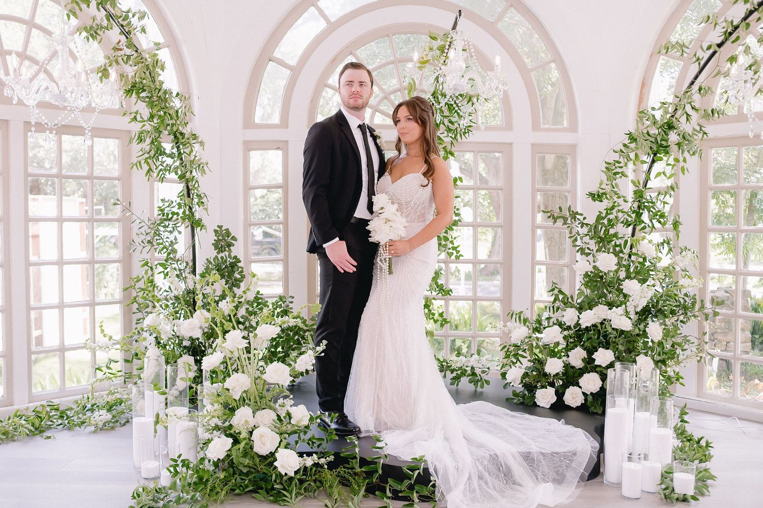 Bright conservatory-style wedding venue with arched windows and cascading floral installations.