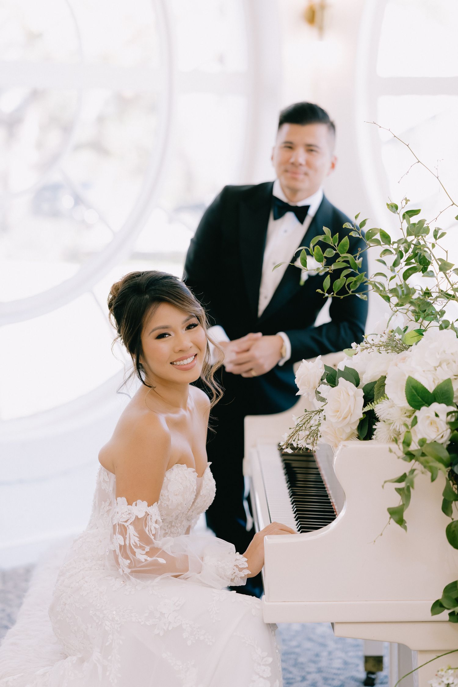 Elegant wedding scene with white grand piano decorated with greenery in a bright venue.