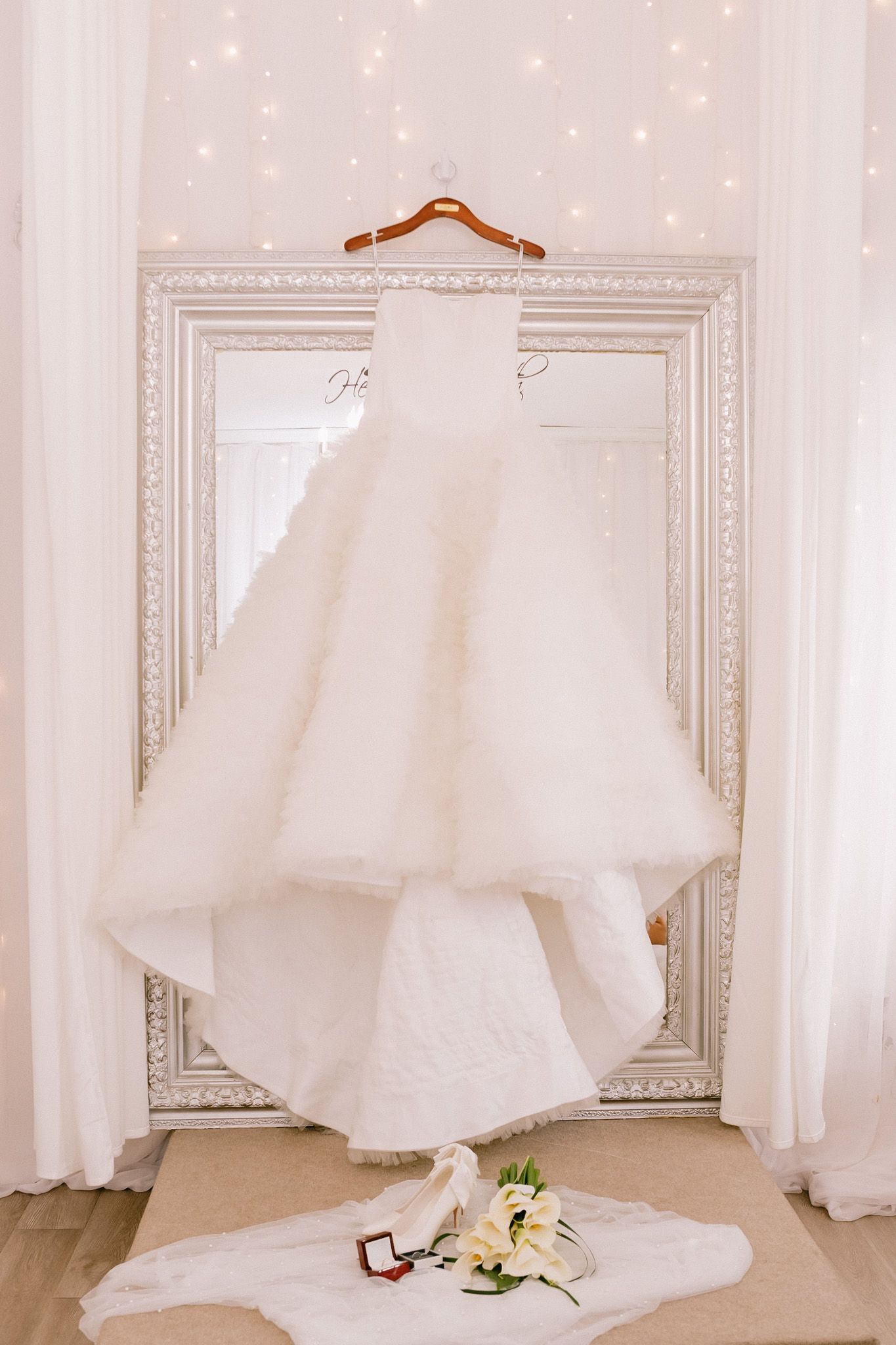 Row of elegant white wedding dresses displayed on hangers against a light-colored wall.