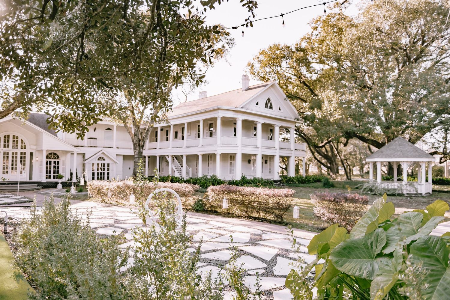 Panoramic view of a grand white wedding venue with string lights and mature trees.