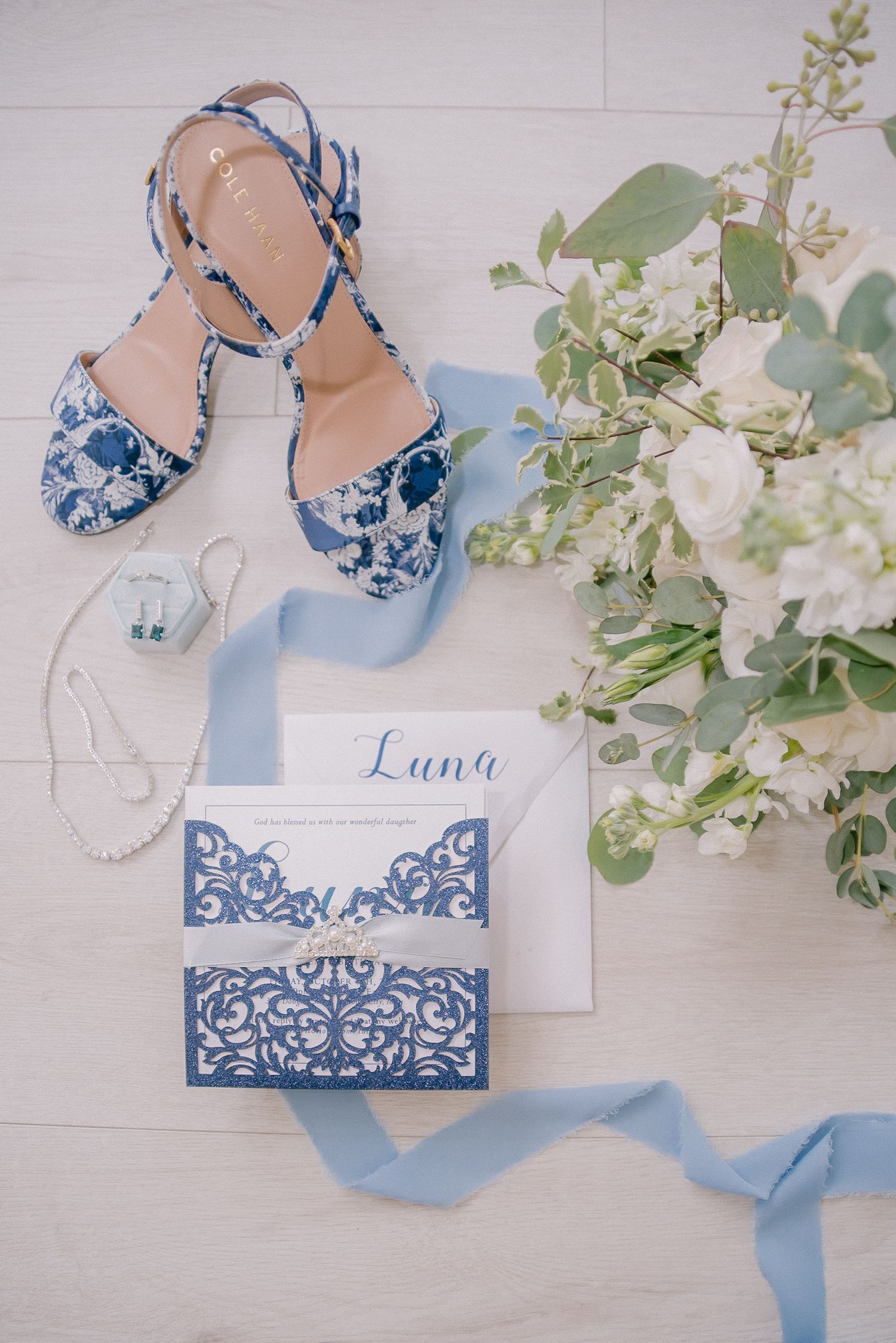Blue and white wedding accessories including lace invitations, shoes and floral decorations.