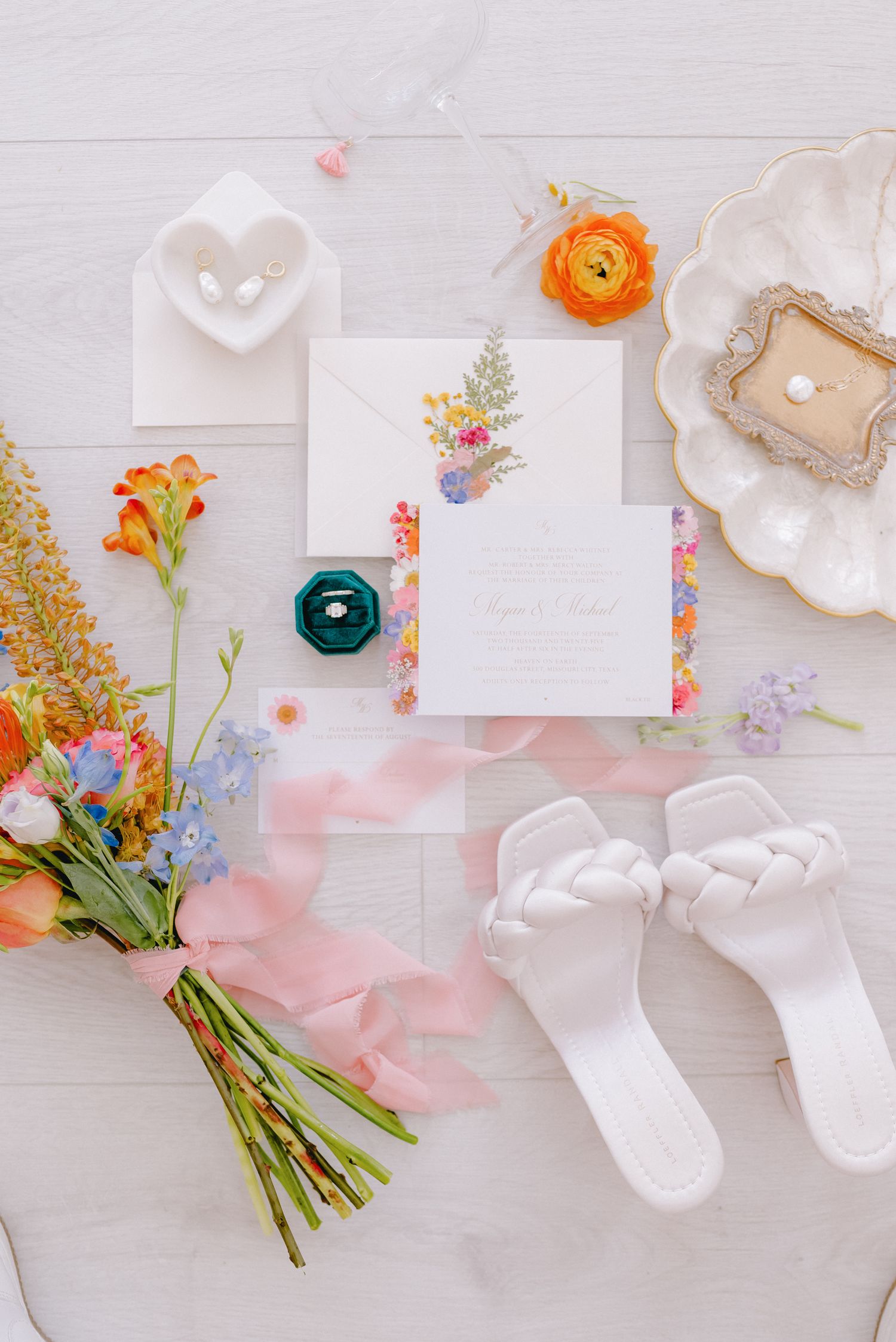 Wedding flatlay with floral invitation, colorful bouquet, white shoes and decorative details.