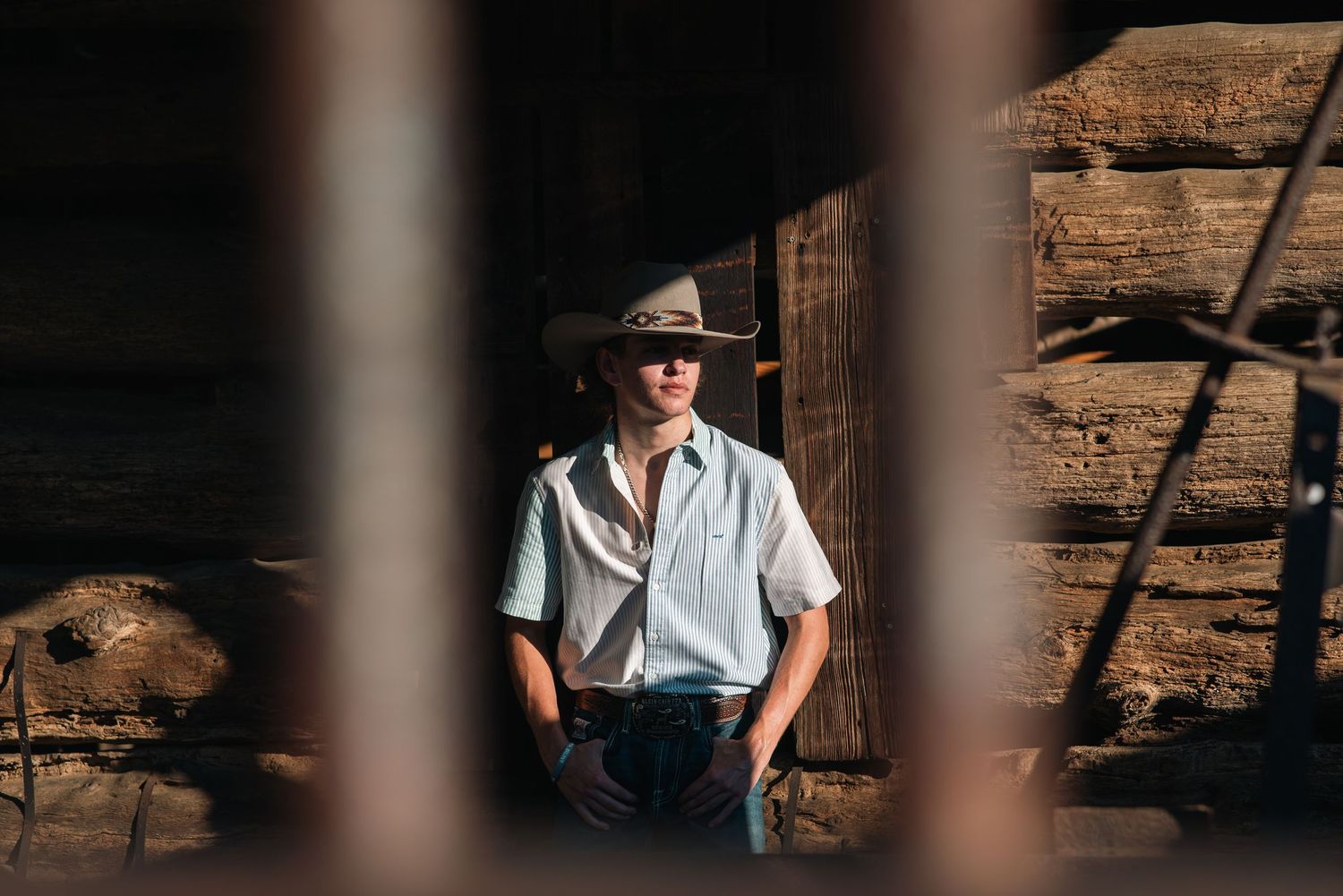 Artistic portrait through wooden beams showing cowboy hat and white shirt.