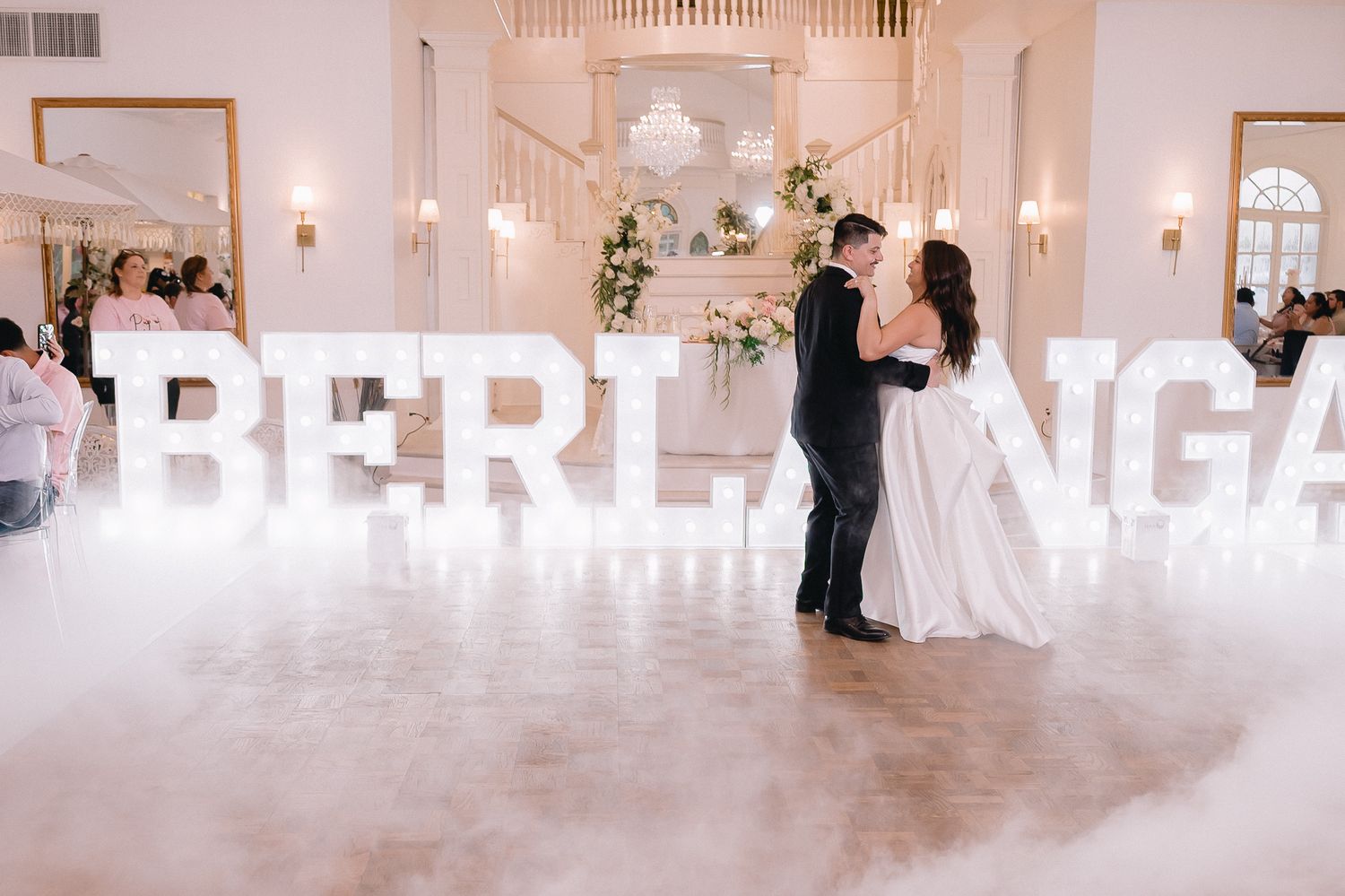 Luxurious white ballroom with crystal chandeliers and illuminated signage.