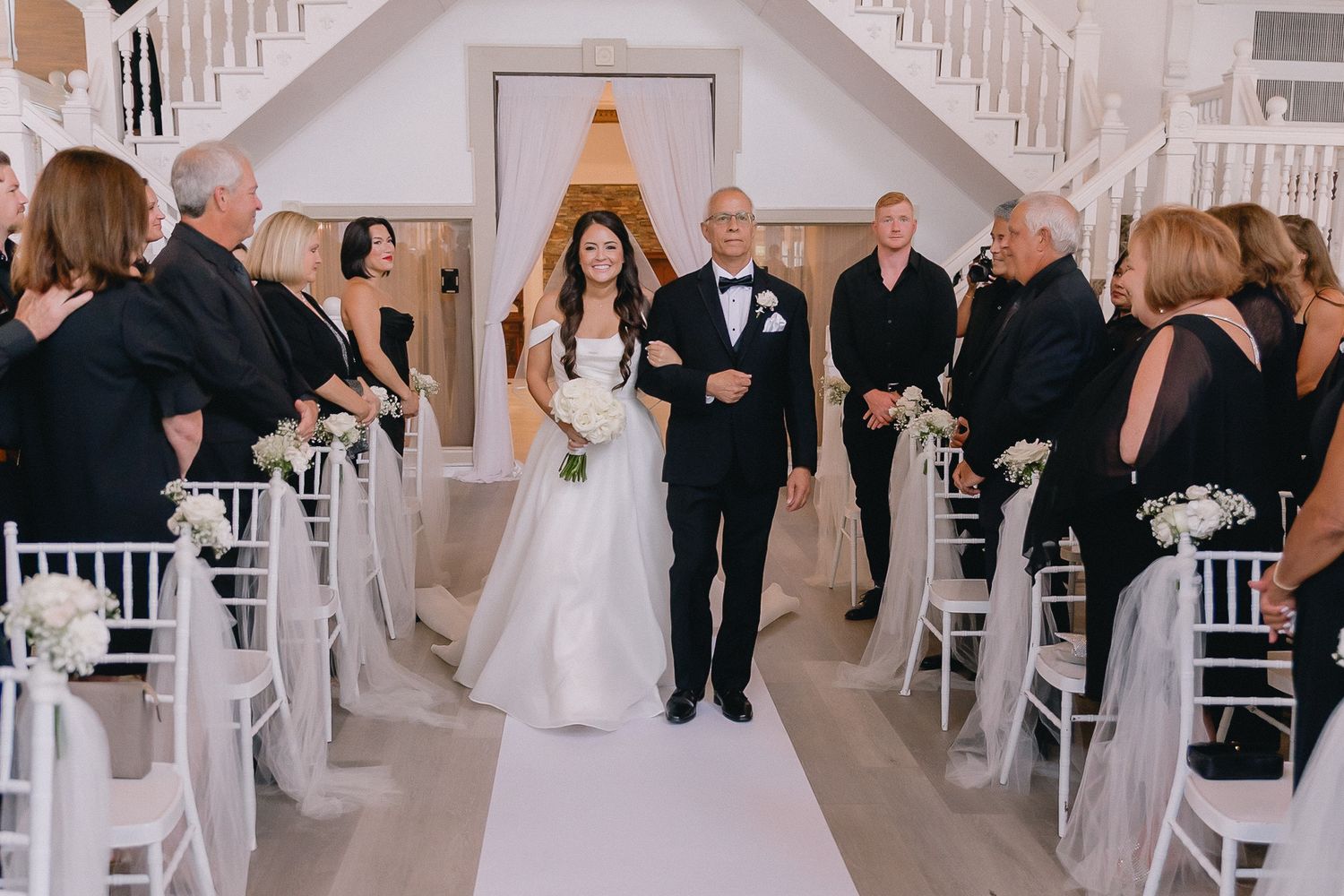Wedding party members arranged in formal poses inside bright white venue with architectural details.