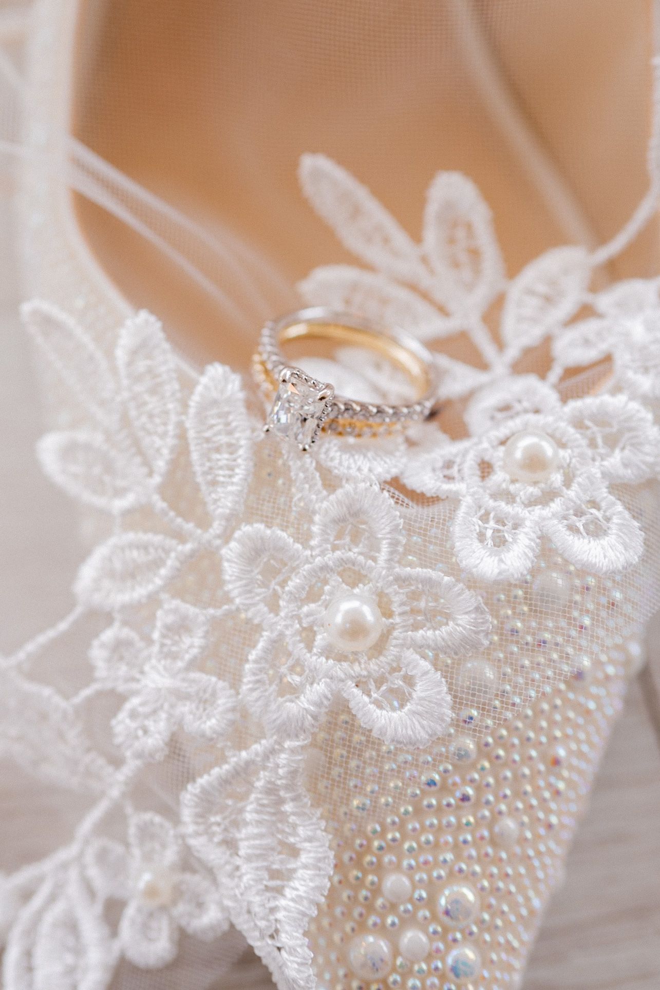 Diamond engagement ring resting on delicate white lace and pearl beaded fabric.