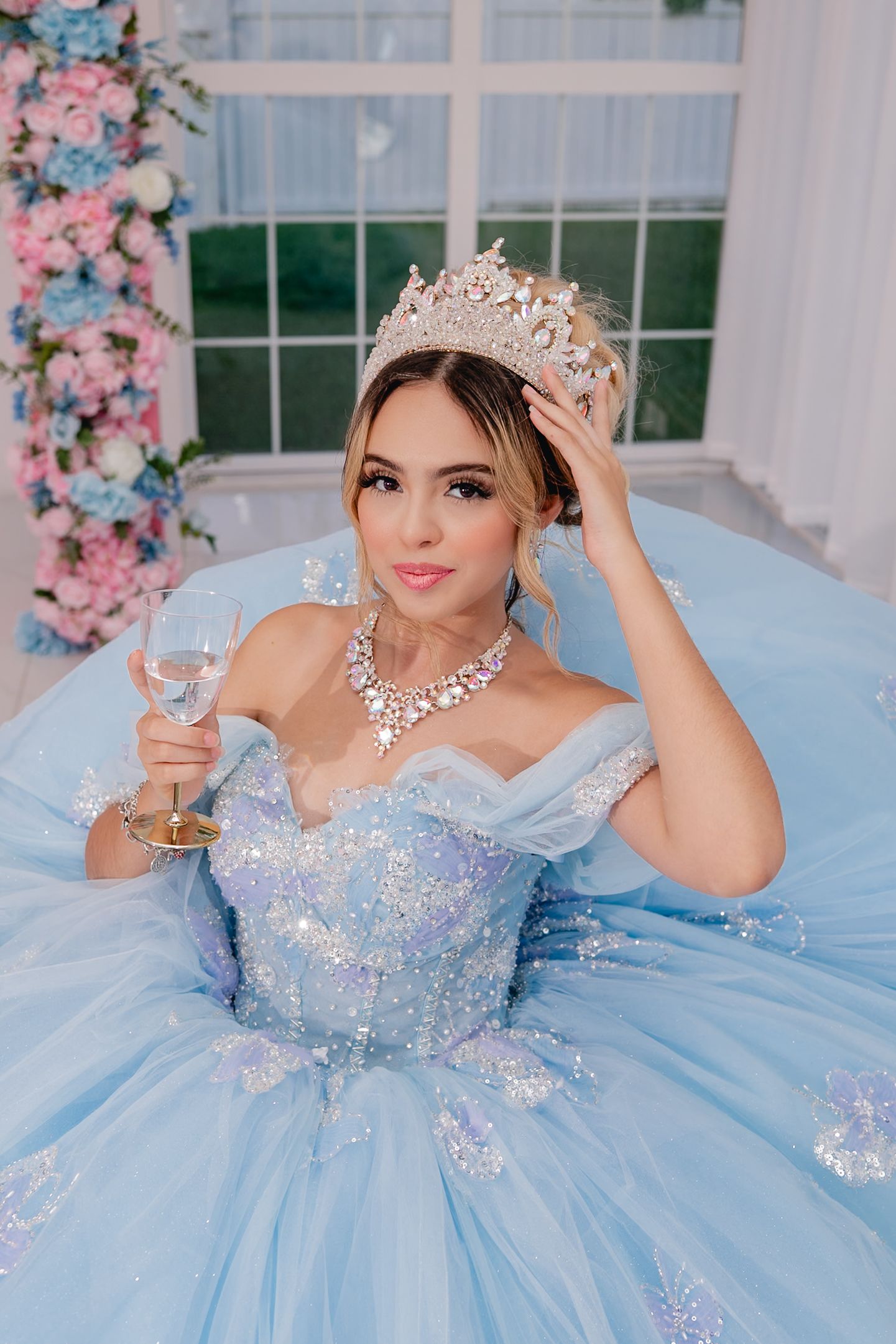 A dreamy blue quinceañera dress with crystal embellishments and a voluminous tulle skirt in a bright white venue.