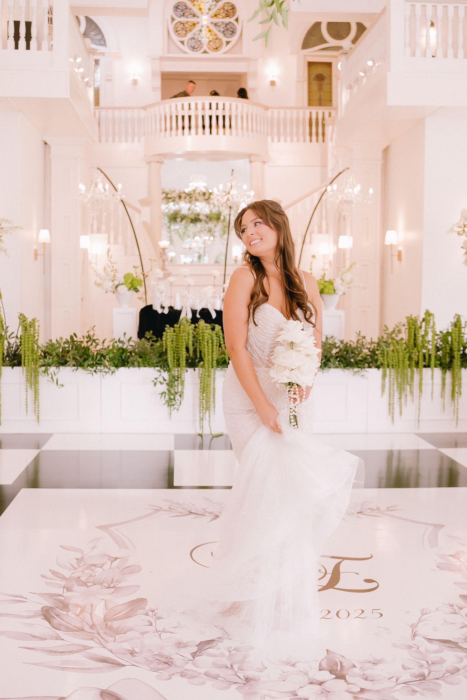 Elegant white ballroom with chandelier and floral decorations for wedding celebration.