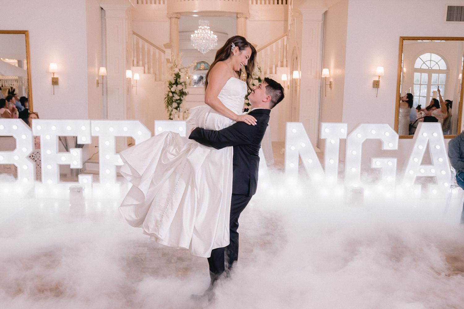 Grand ballroom wedding reception with dramatic lighting and elegant white decor elements.