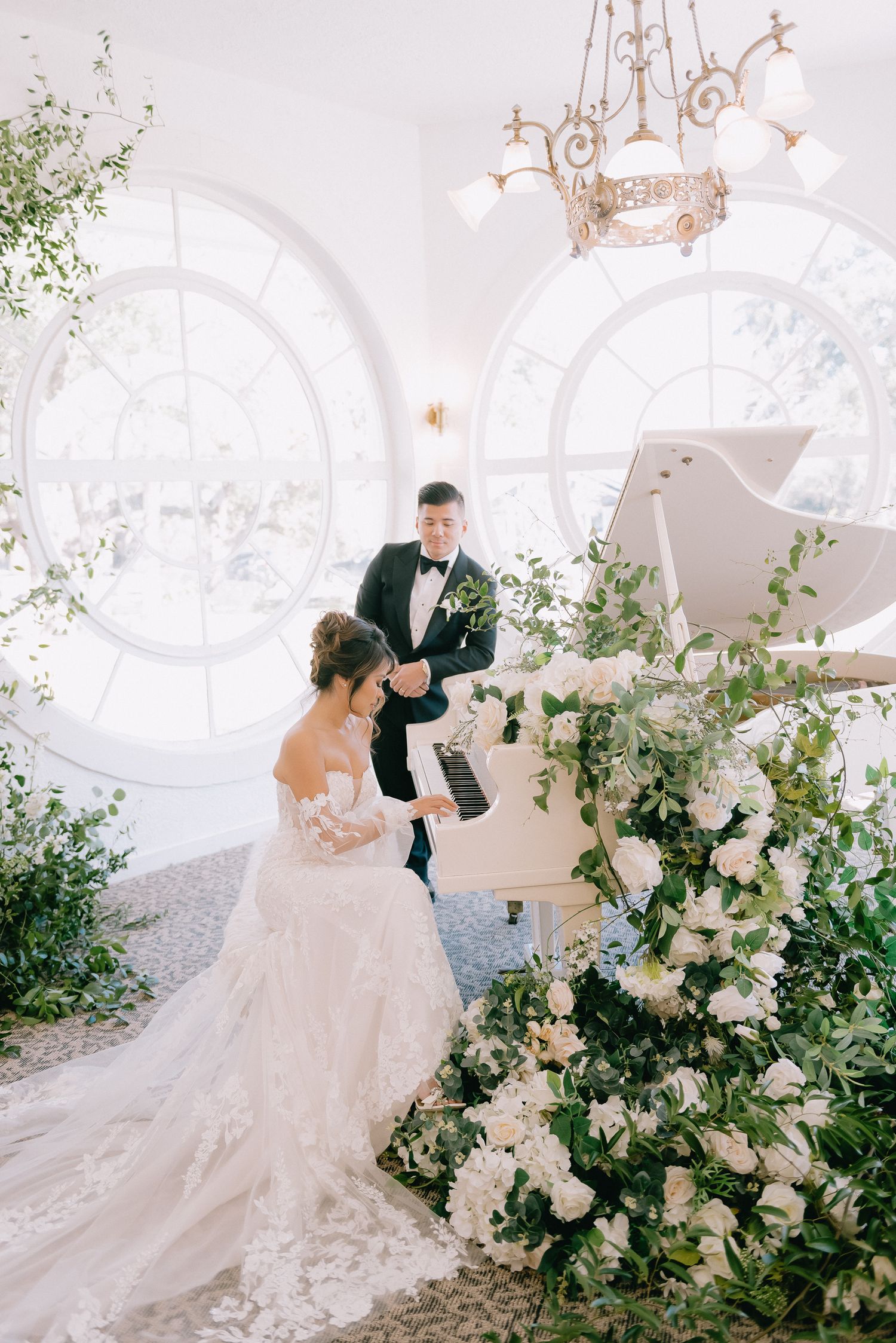Wedding couple surrounded by lush white floral arrangements and greenery in an elegant white venue.