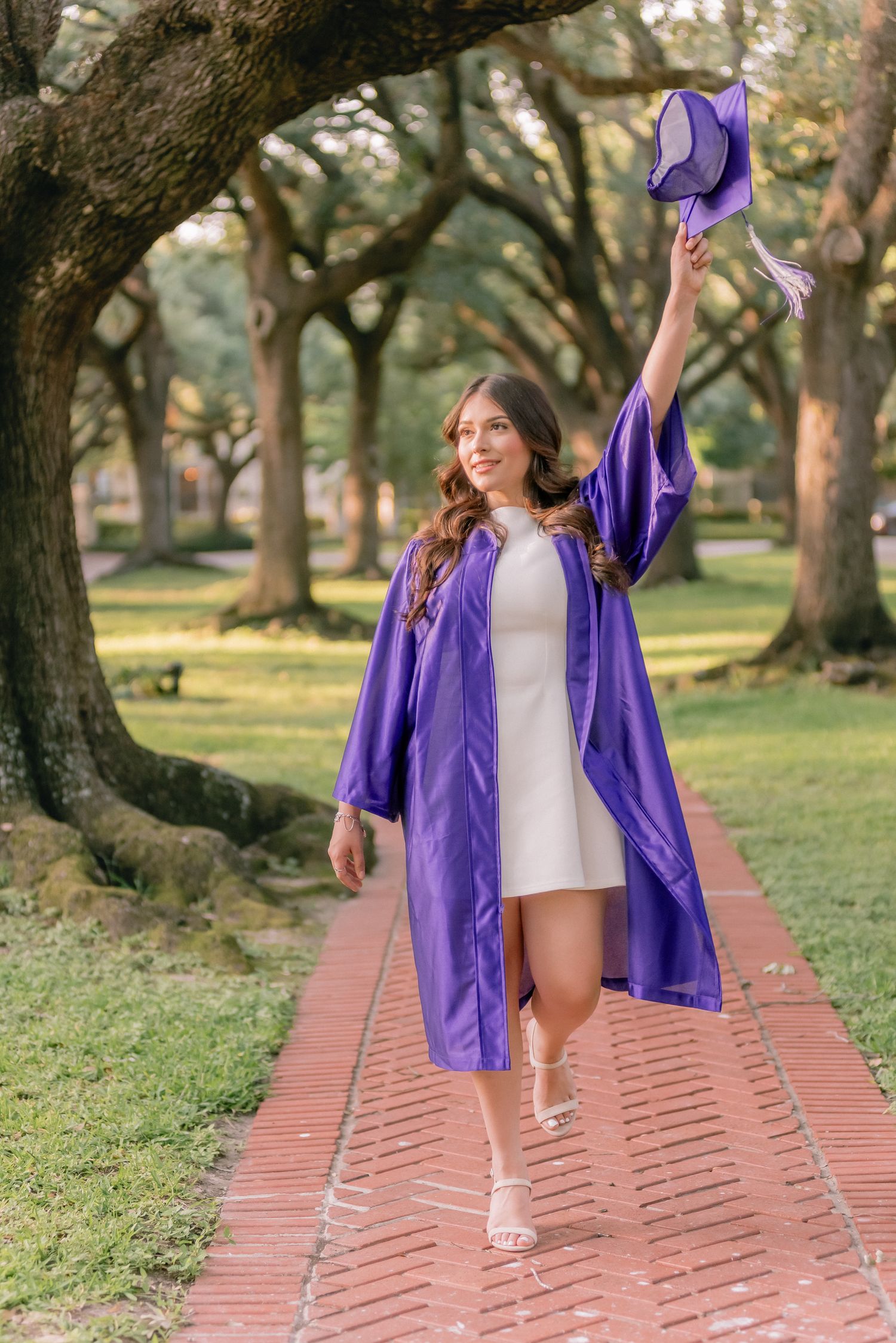 Person walking on brick pathway wearing purple graduation gown in outdoor setting.