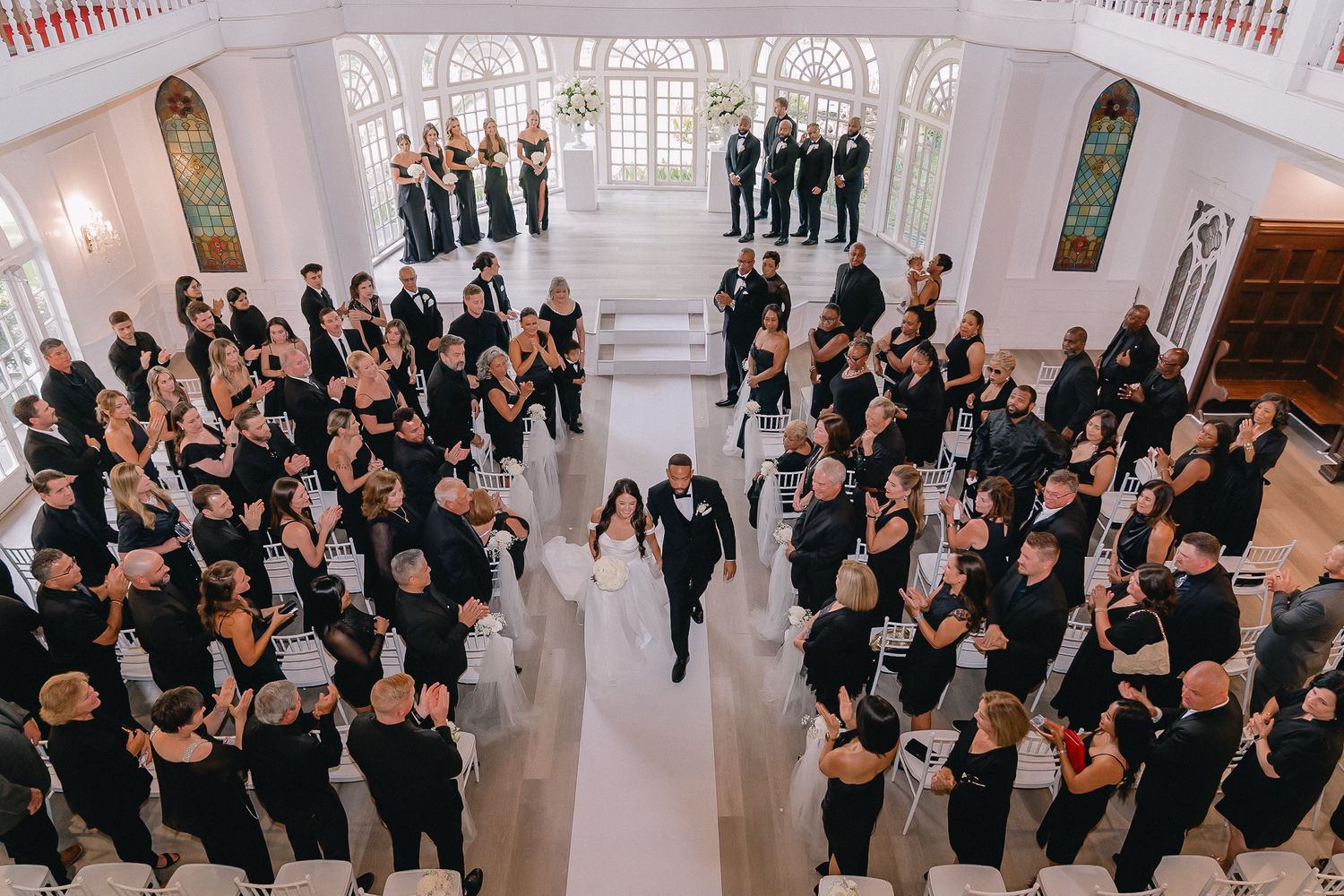 Aerial view of wedding celebration in grand white ballroom with formal dressed attendees.