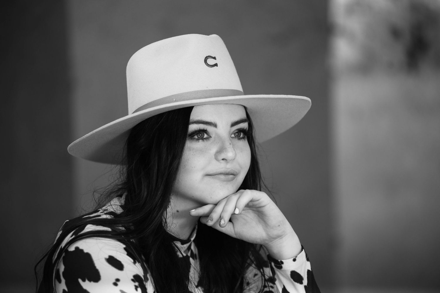 A black and white portrait featuring a western-style hat and cow print clothing.