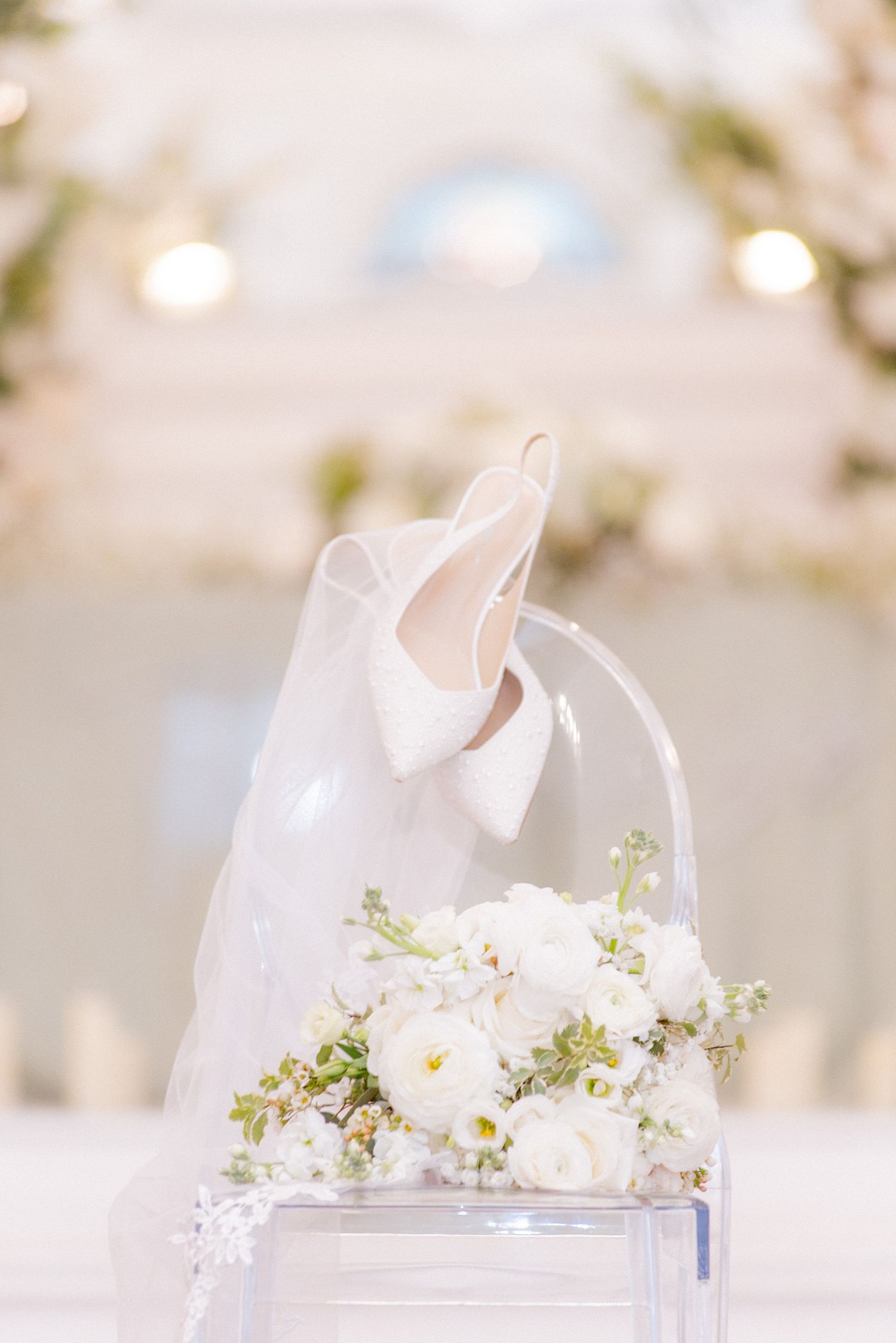 White wedding shoes adorned with delicate floral decorations and greenery on a light background.