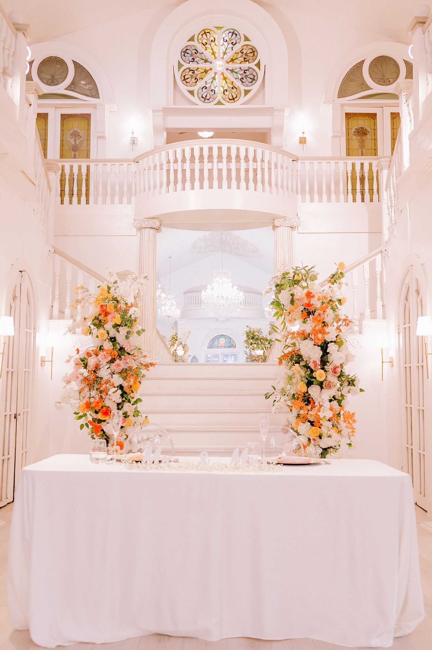 Wedding reception setup in white ballroom with peach floral arrangements and elegant table settings.