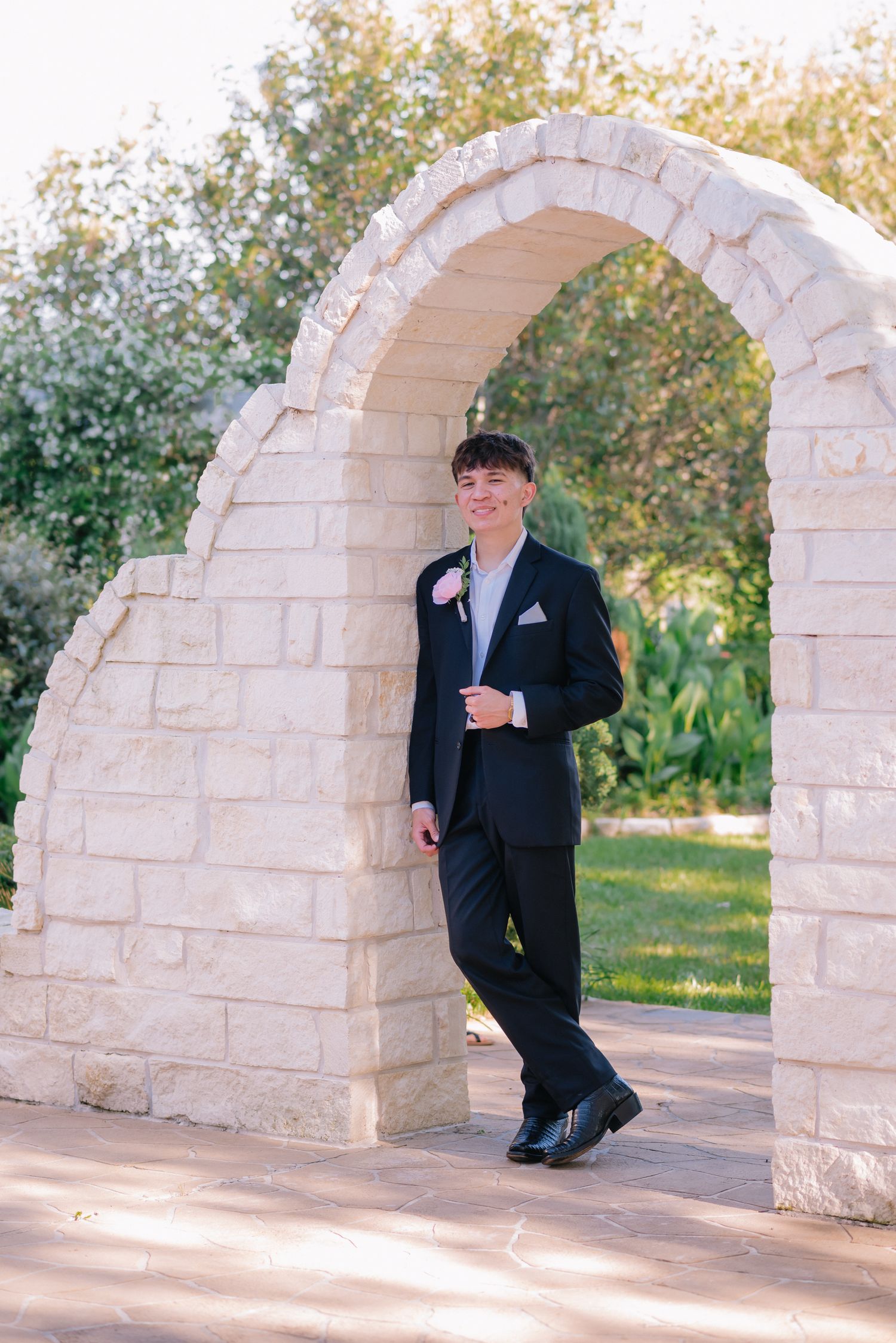 Figure in dark suit posing near decorative white stone archways outdoors.