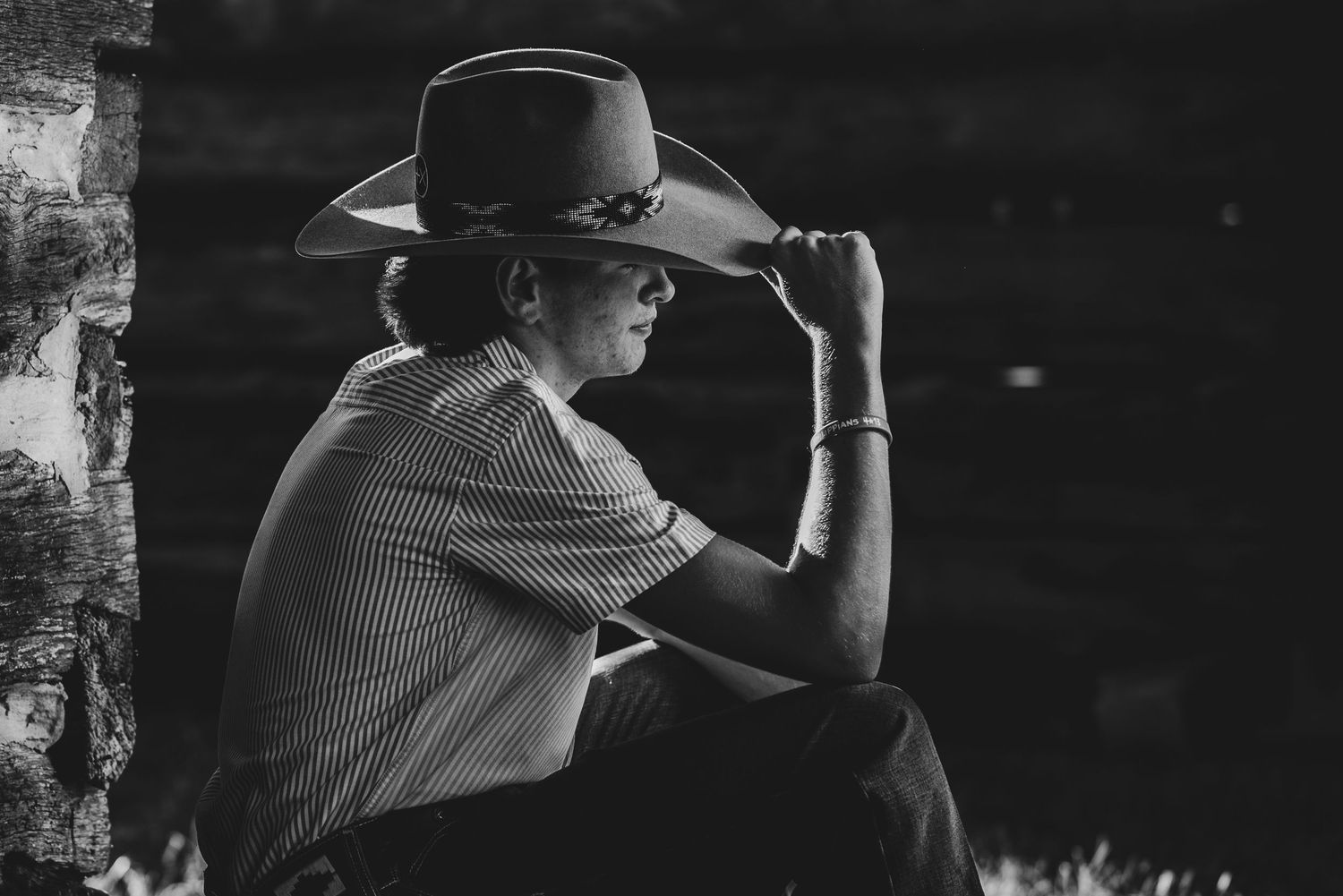 Dramatic side profile of person adjusting cowboy hat in black and white photography.
