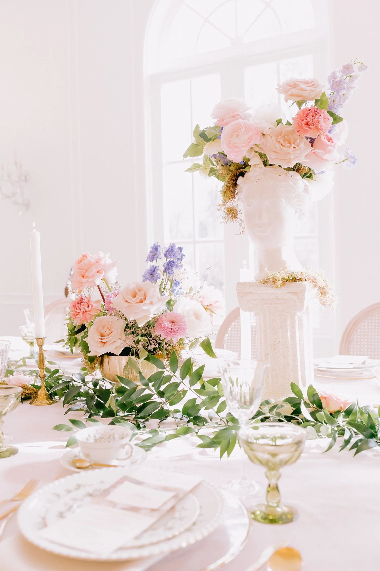 Romantic table setting with pink roses, greenery and crystal glassware in soft natural light.