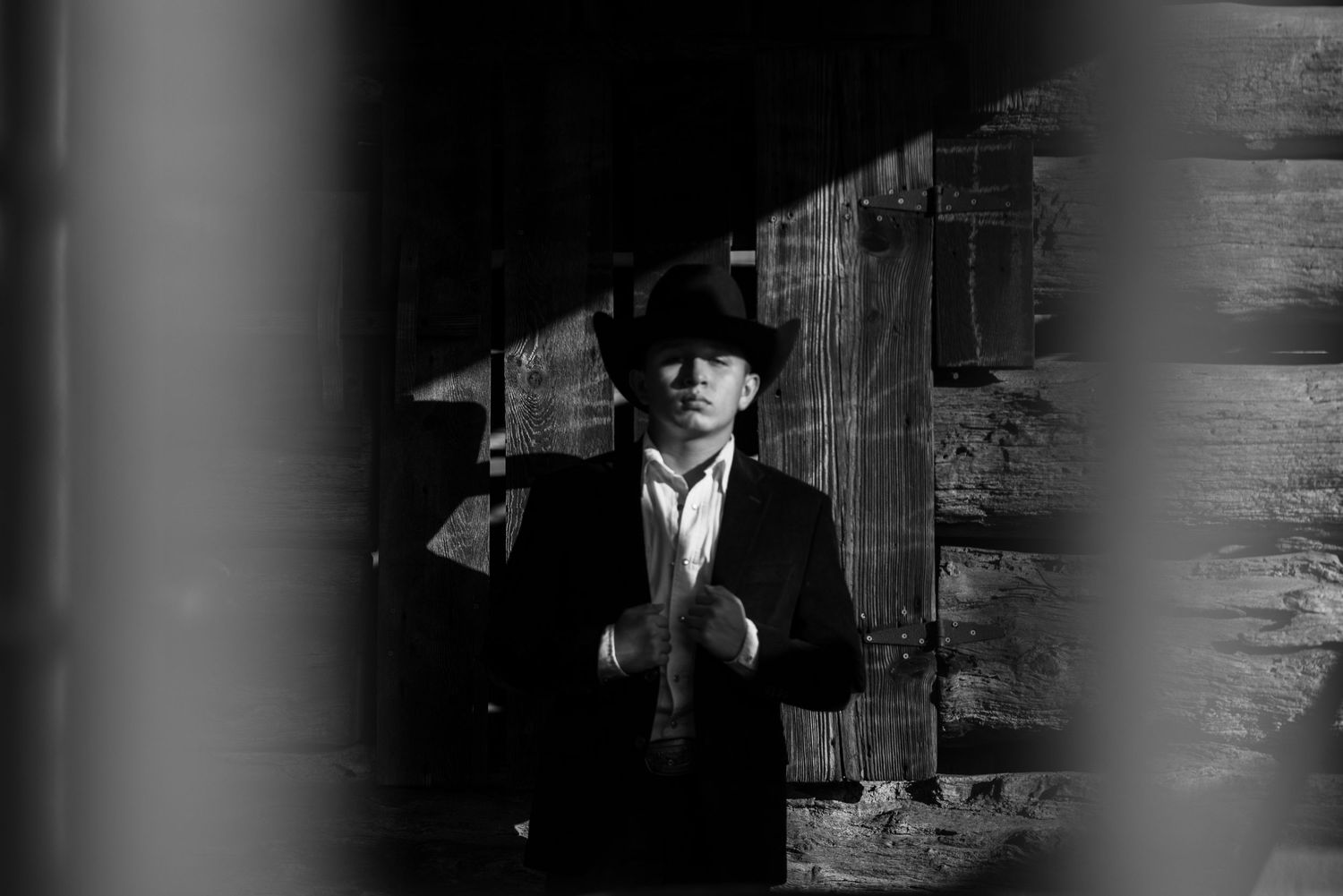 Dramatic black and white portrait of someone in cowboy attire against dark background.