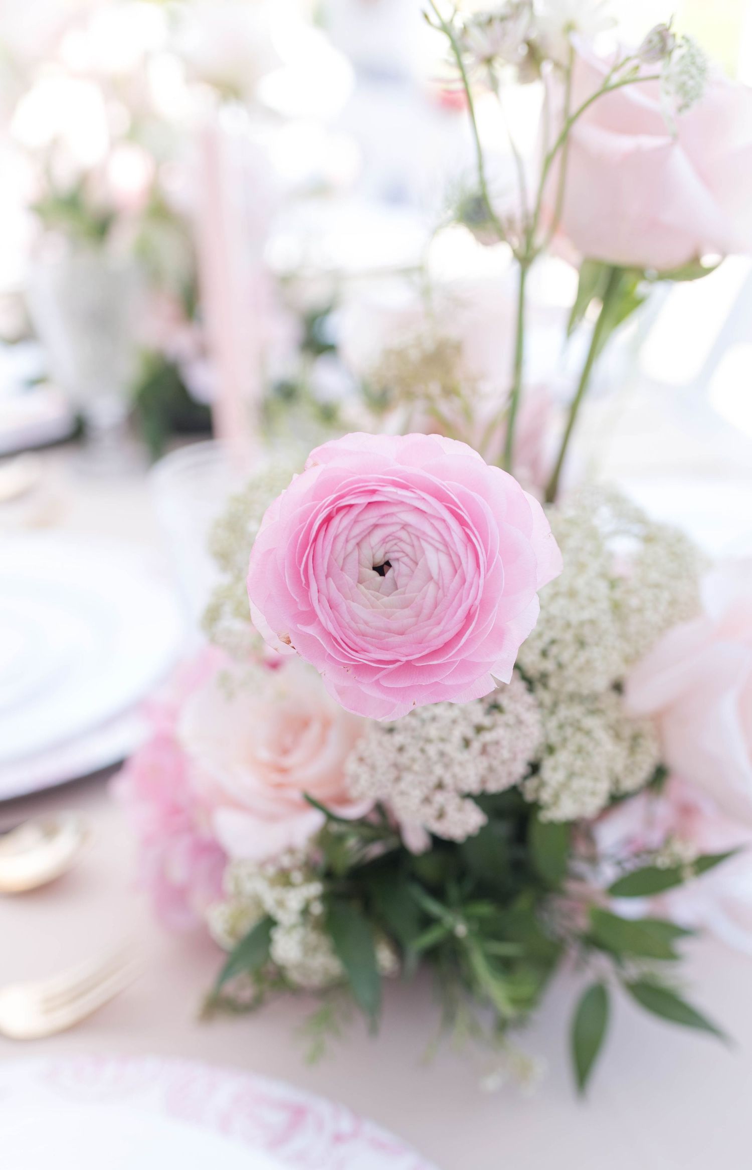 Delicate pink ranunculus and white floral centerpiece arrangement on light pink table setting.