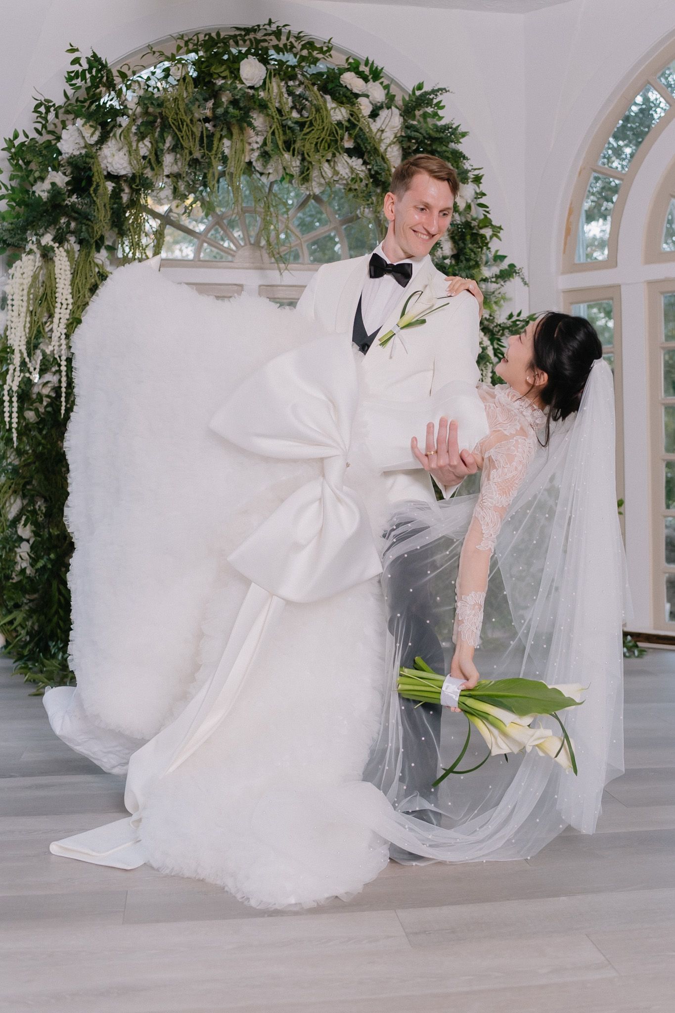 Romantic wedding couple dancing in an elegant white venue decorated with greenery.