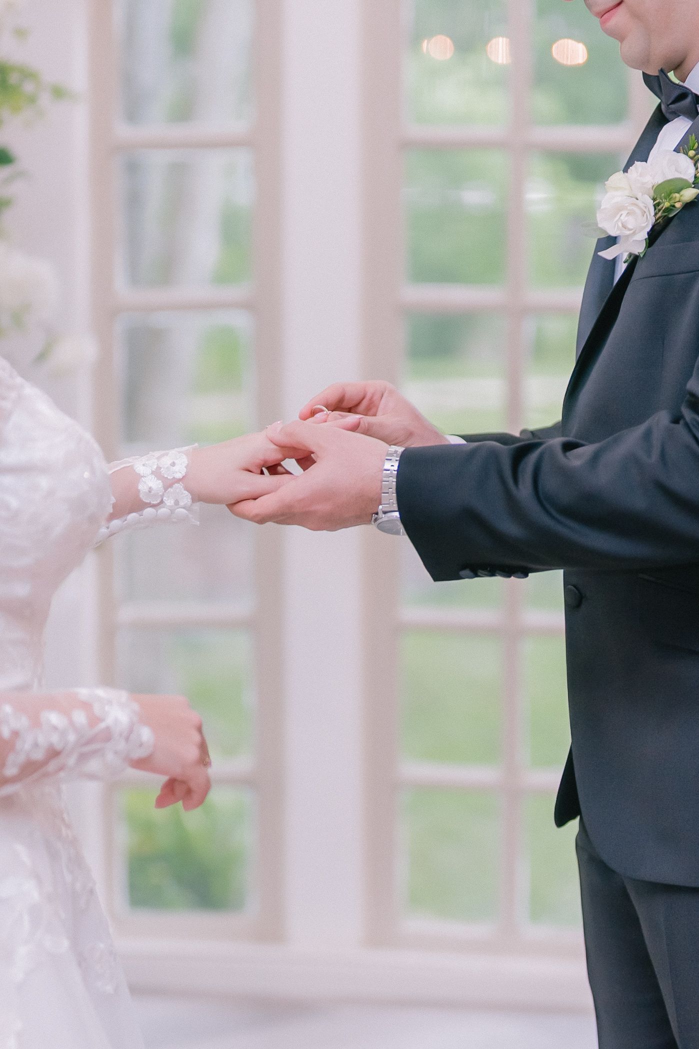 Close-up of hands exchanging rings during wedding ceremony in bright indoor setting.