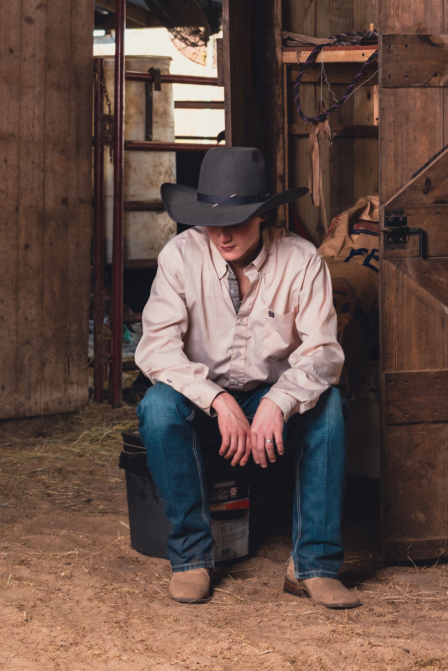 Rustic barn interior scene with cowboy seated on wooden structure.