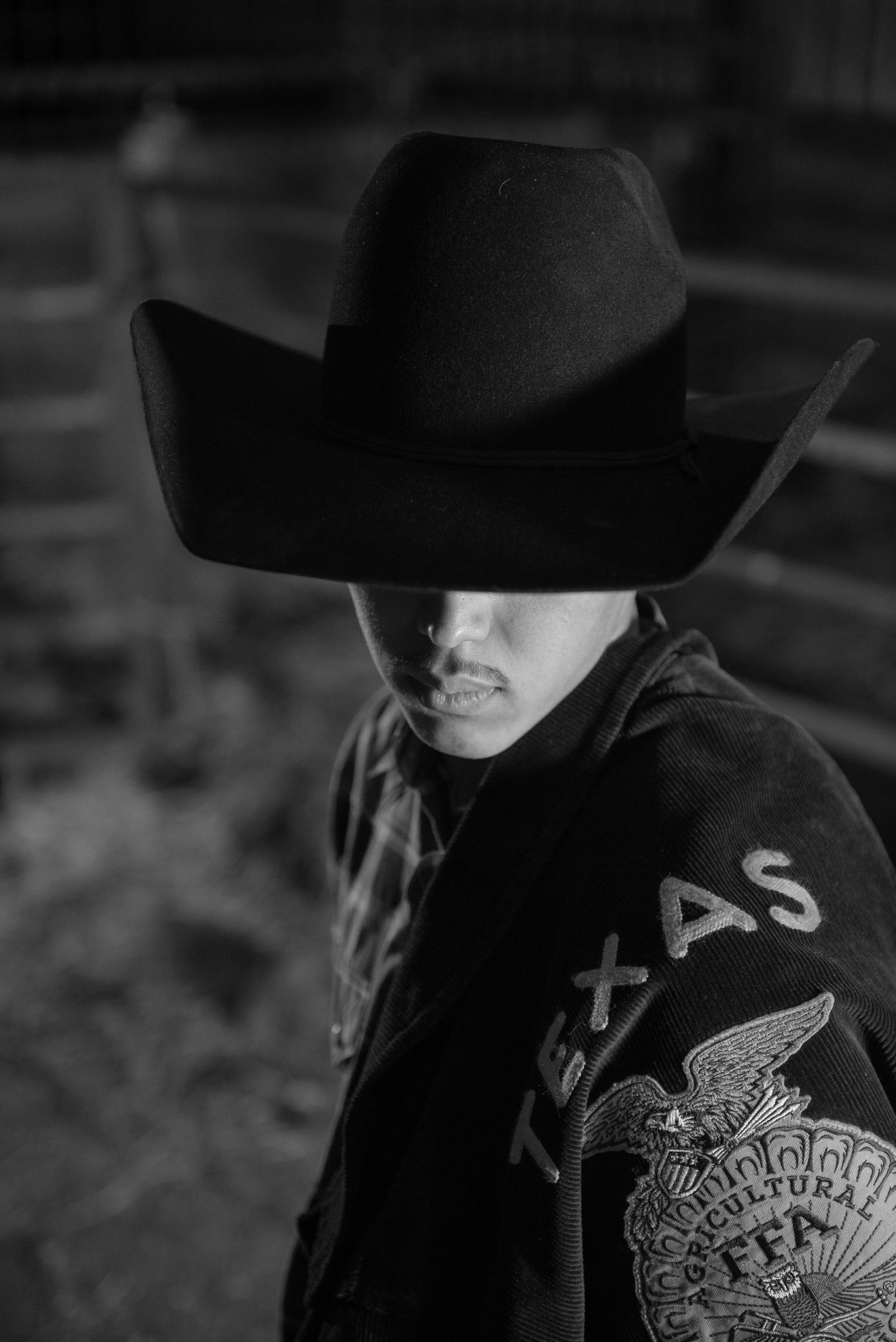 Person wearing black cowboy hat and FFA jacket in dramatic black and white portrait.