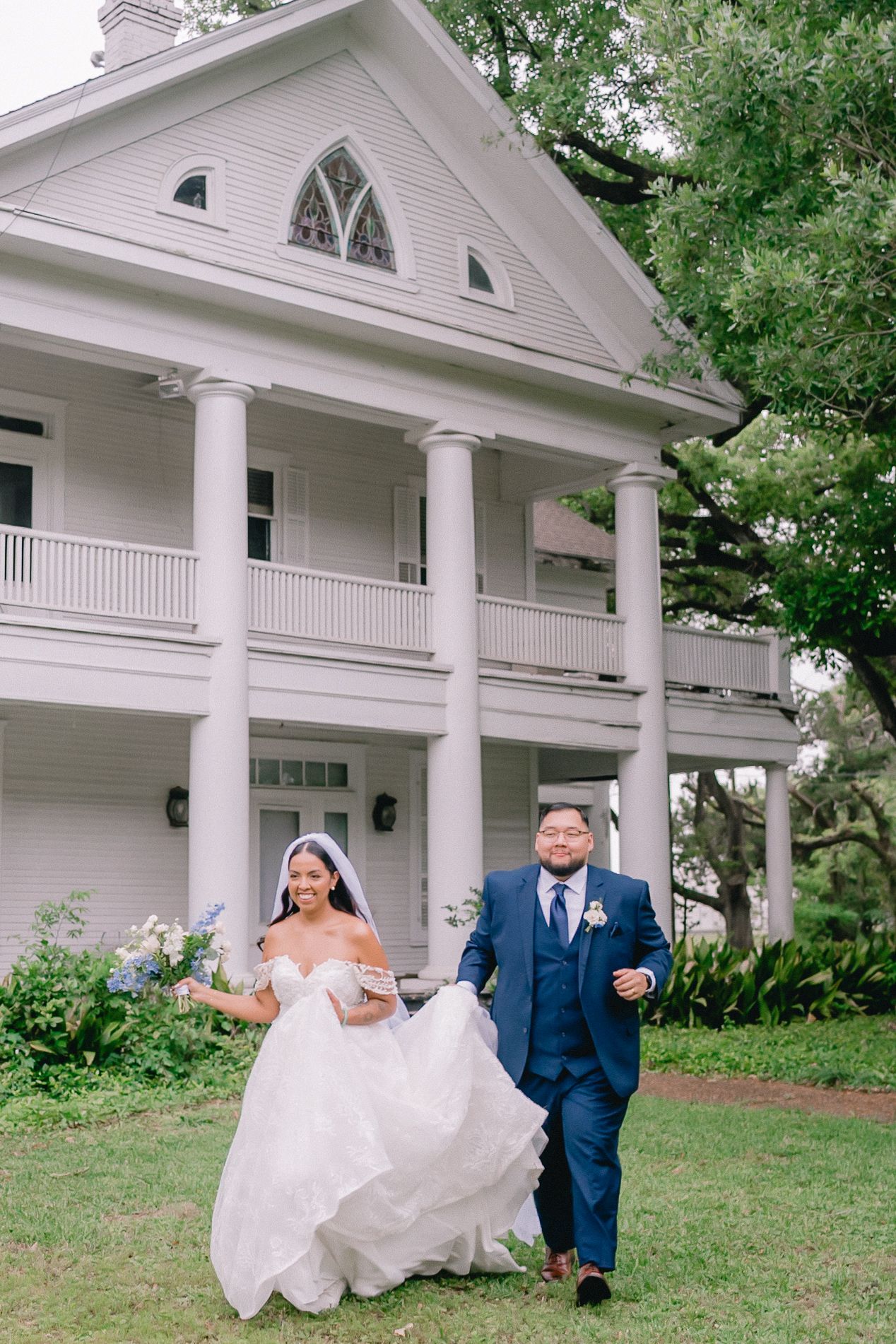 Classic white colonial style mansion serves as backdrop for wedding photo on manicured lawn.